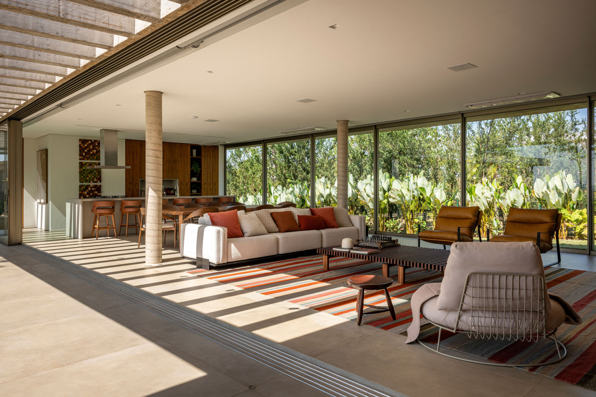Open living space with concrete columns and floor-to-ceiling glass overlooking planted garden beds
