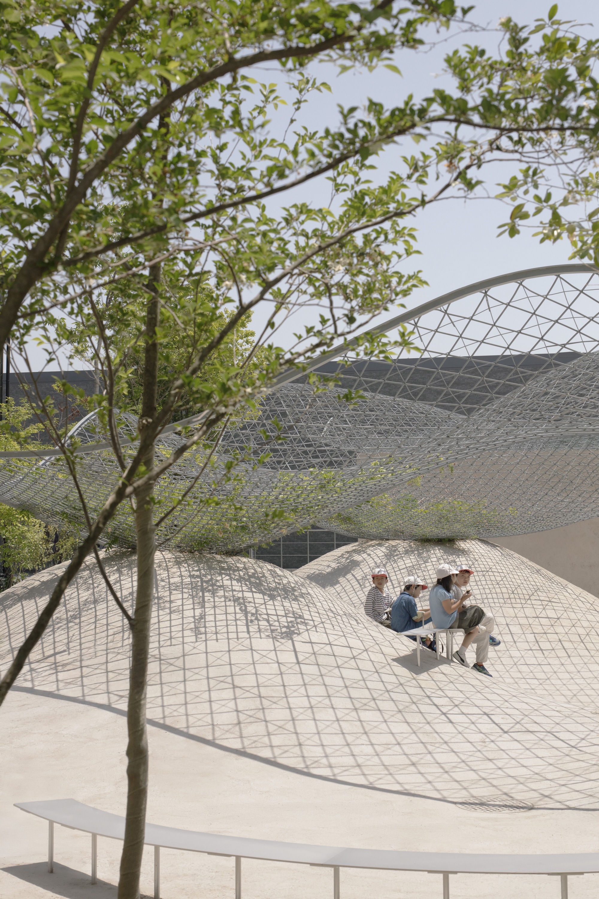 Two visitors seated in a sunken tiled courtyard framed by spring foliage and metal canopy
