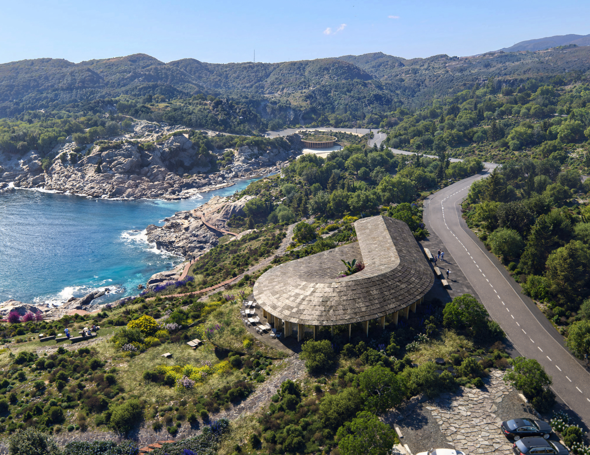Drone view of a curved pavilion with shingle roof beside a coastal road and blue water