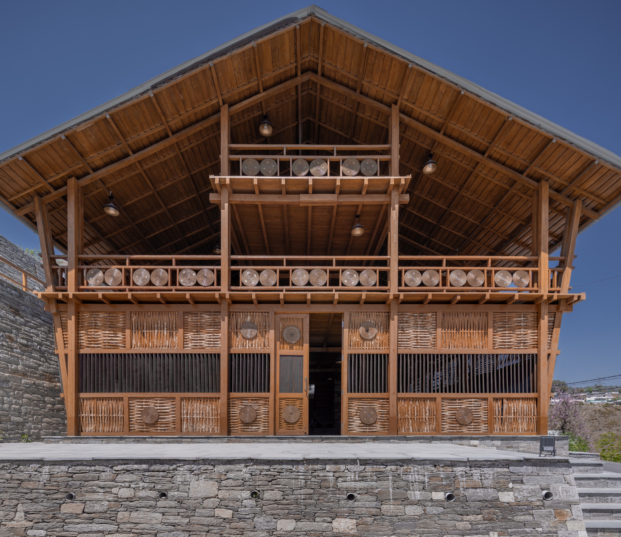 Front elevation of the timber-framed gable with woven bamboo screens and carved circular motifs at twilight