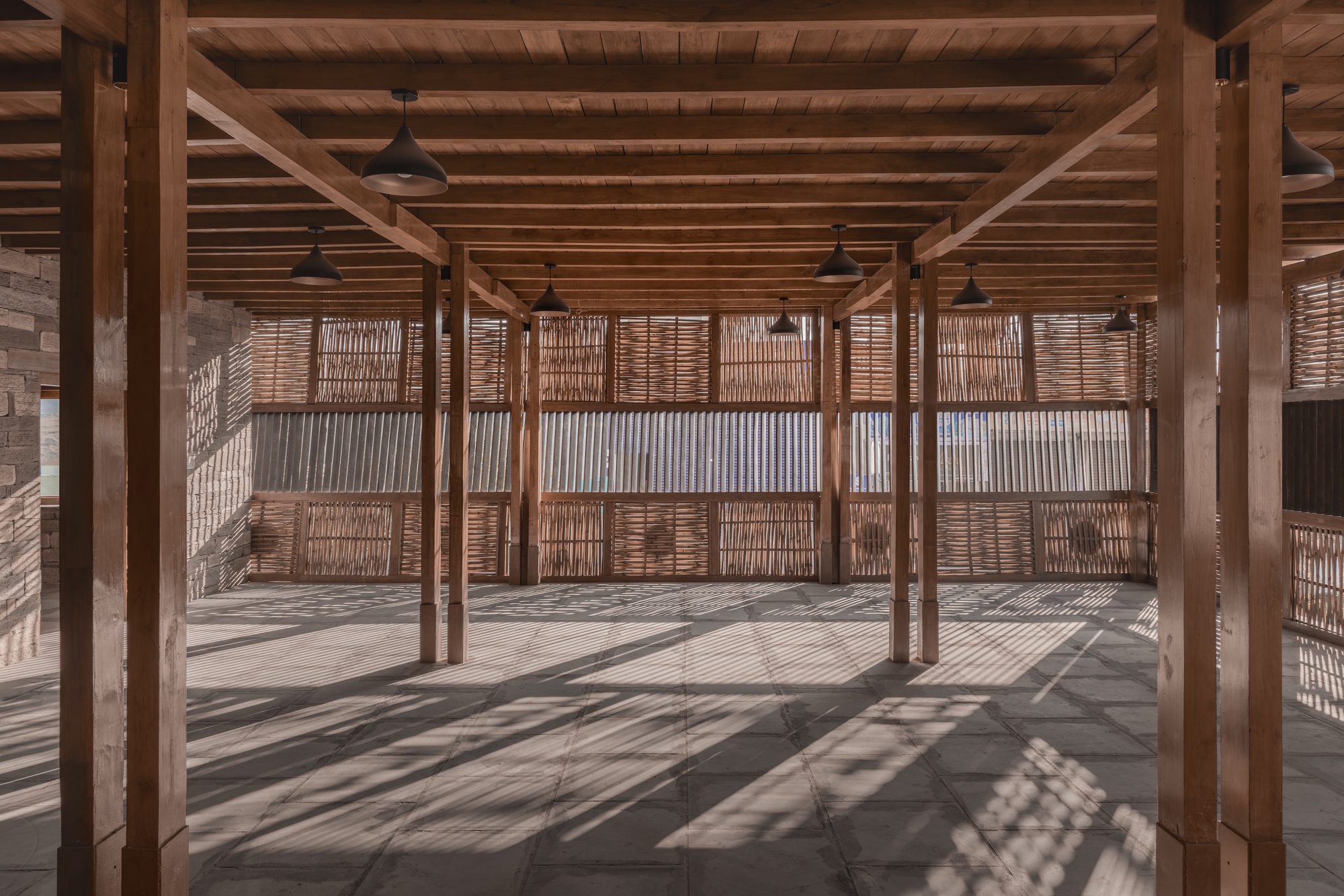 Open space with timber columns and perforated screening panels casting dappled shadows across the floor
