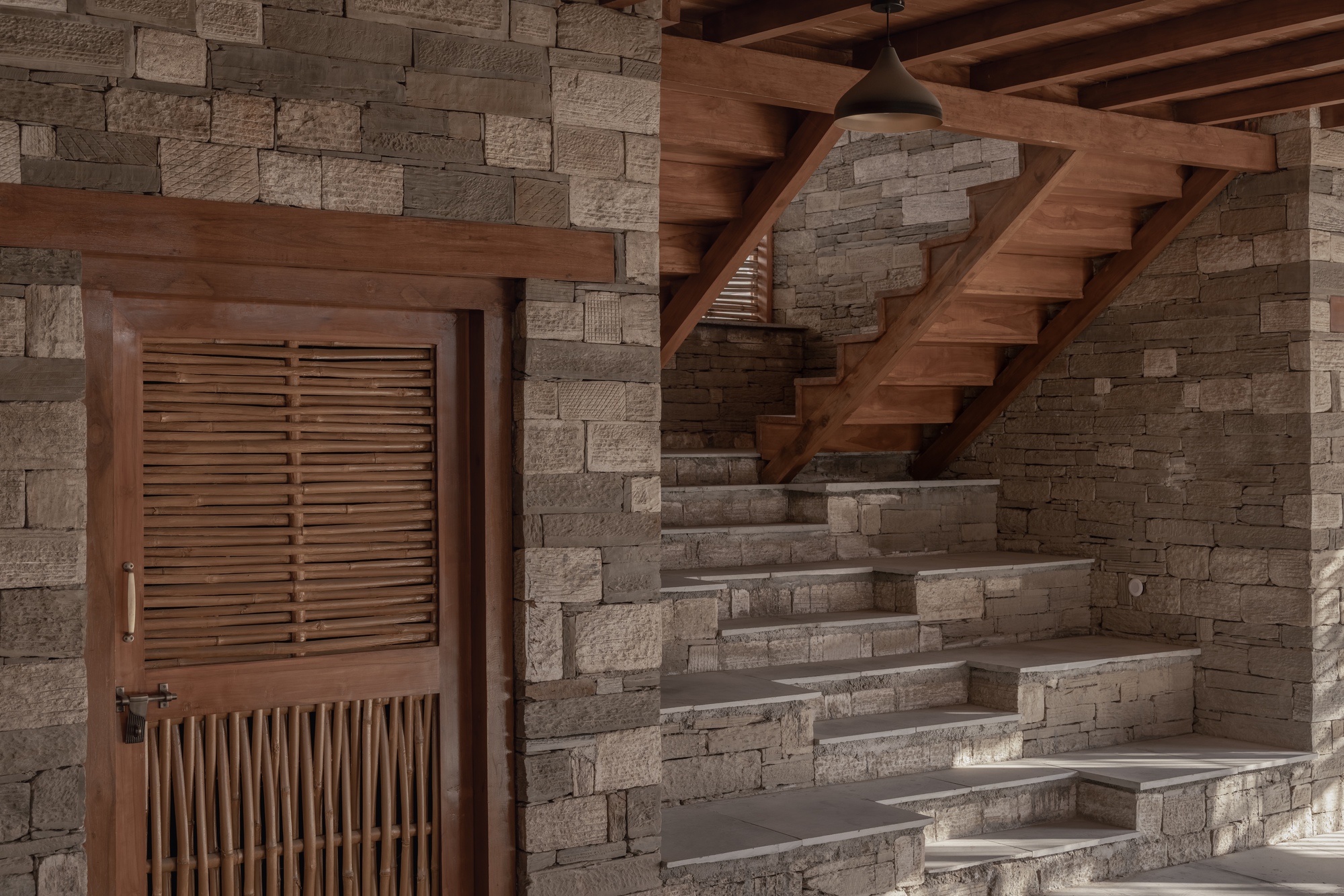 Stone staircase rising along the textured wall with timber door and louvered screen below