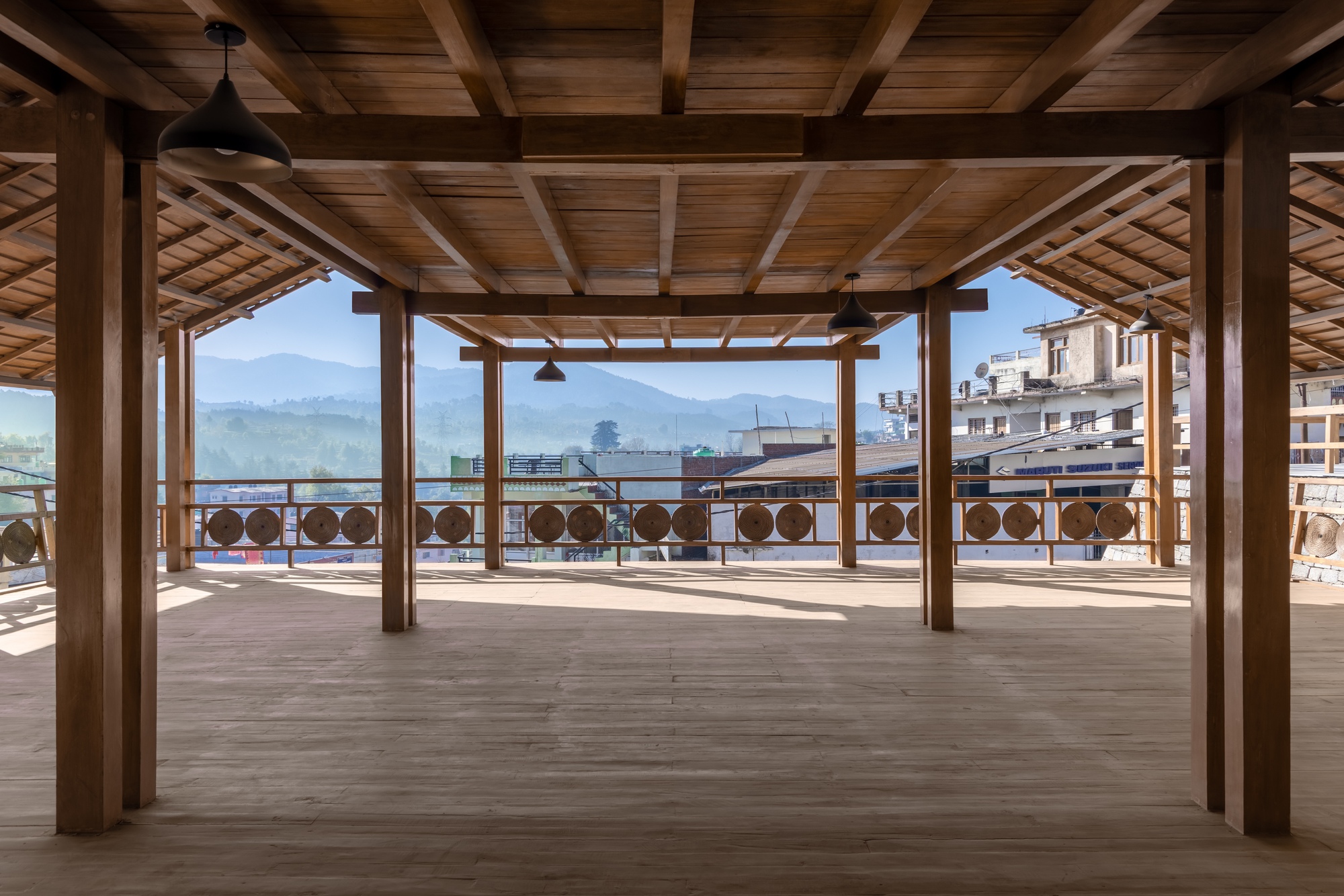 Open timber-framed pavilion with wooden deck and circular balustrade overlooking distant mountain ranges