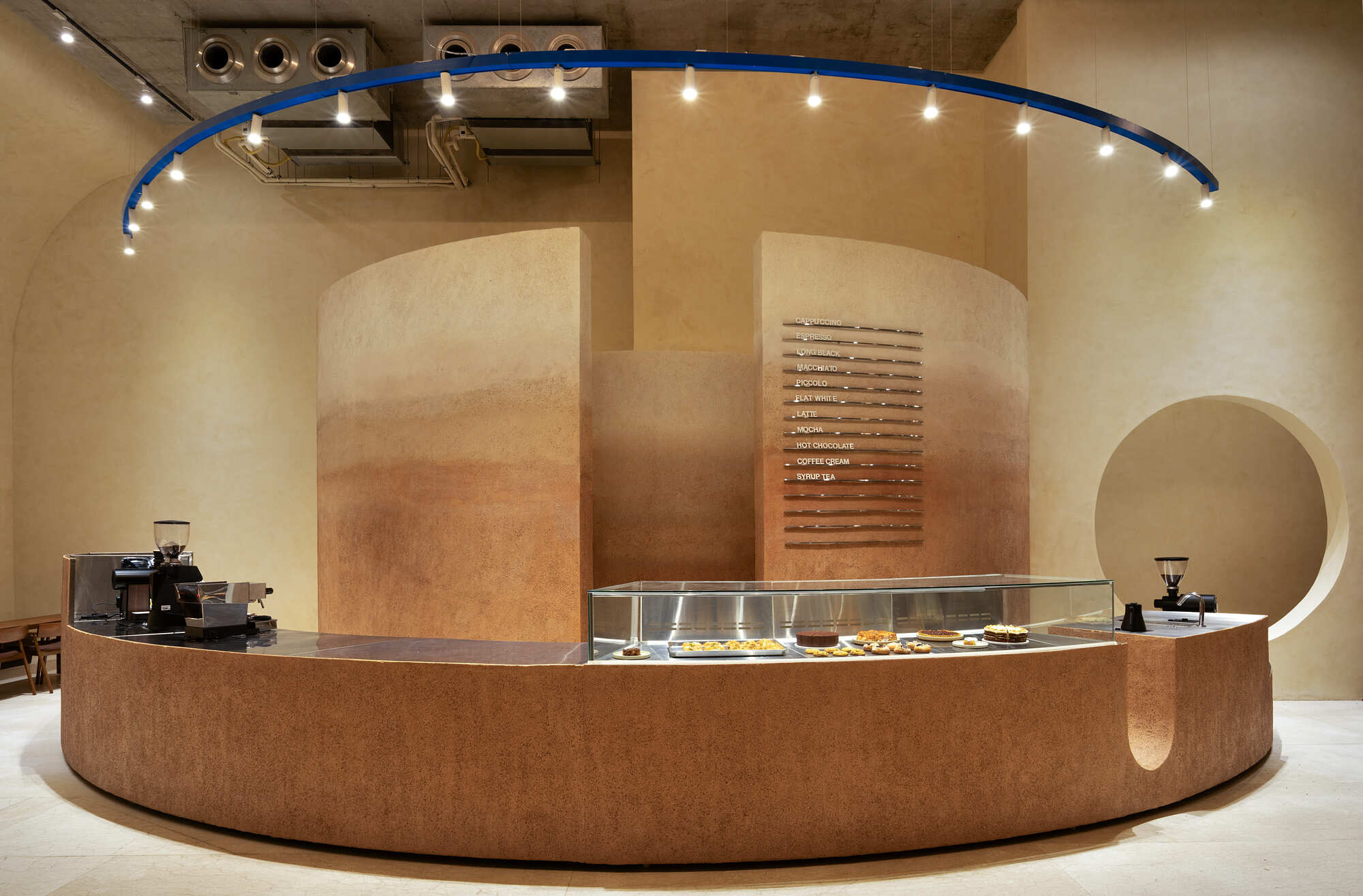 Curved cork-clad service counter with blue lighting rail beneath exposed concrete ceiling