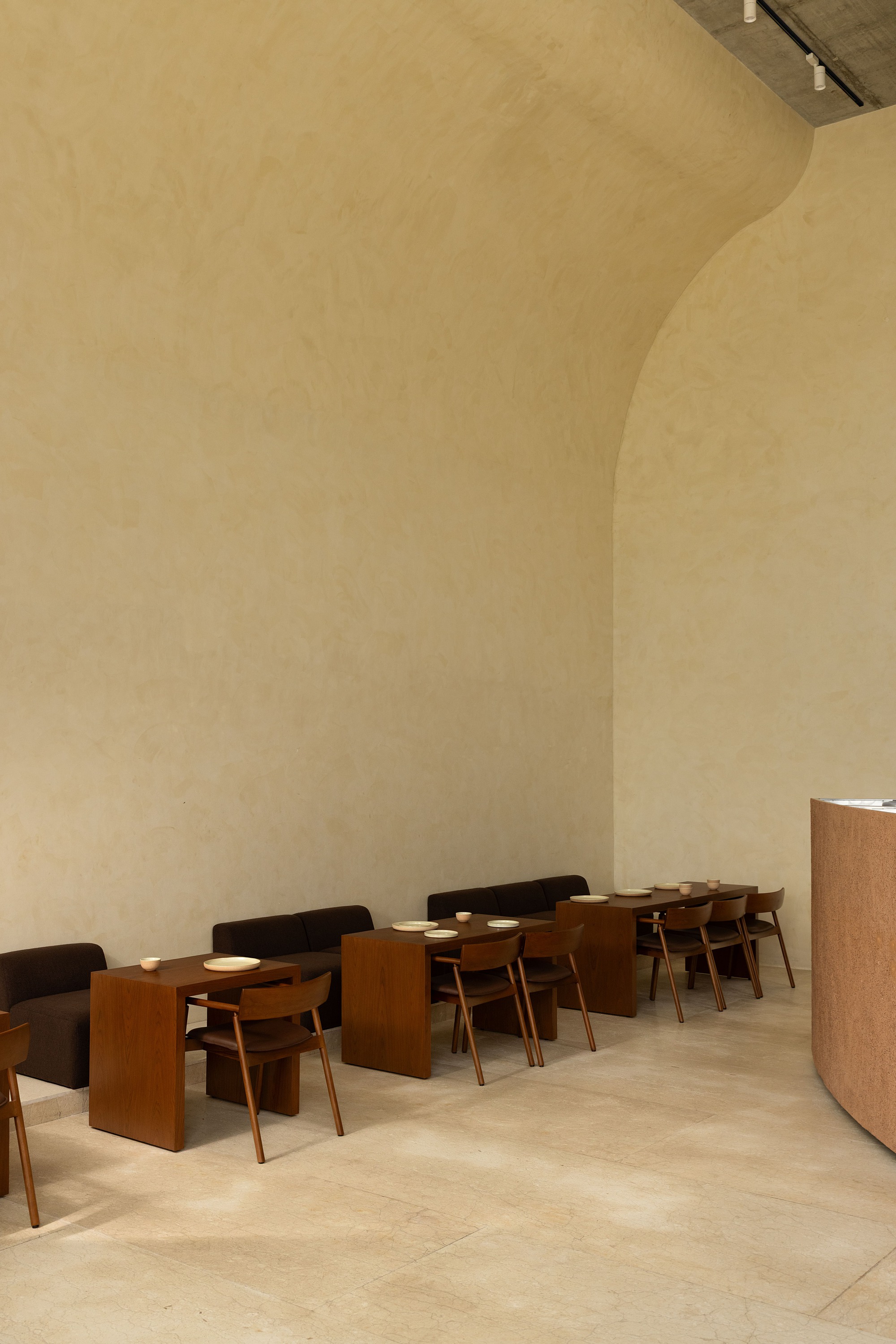 Row of timber dining tables and chairs beneath a curved plaster ceiling in soft light