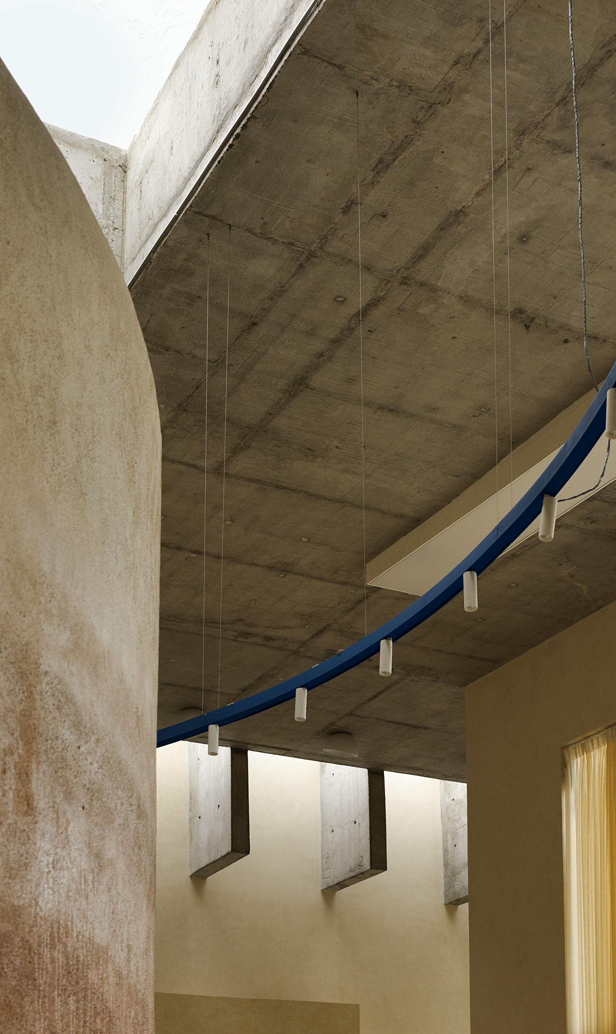 Suspended blue metal handrail with pendant lights below the board-formed concrete ceiling