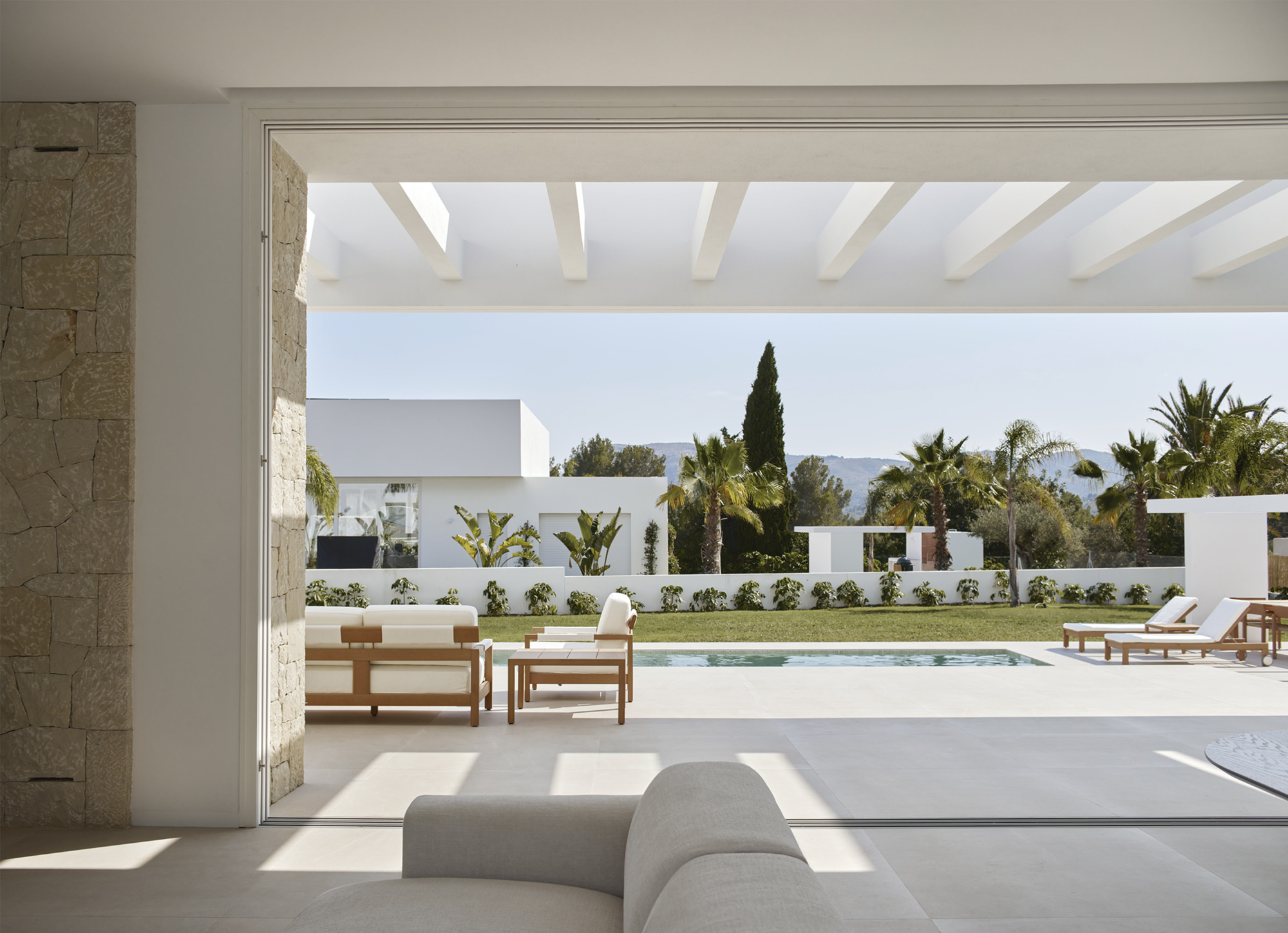 Interior view through open sliding doors to pool terrace with palm trees and cypress beyond