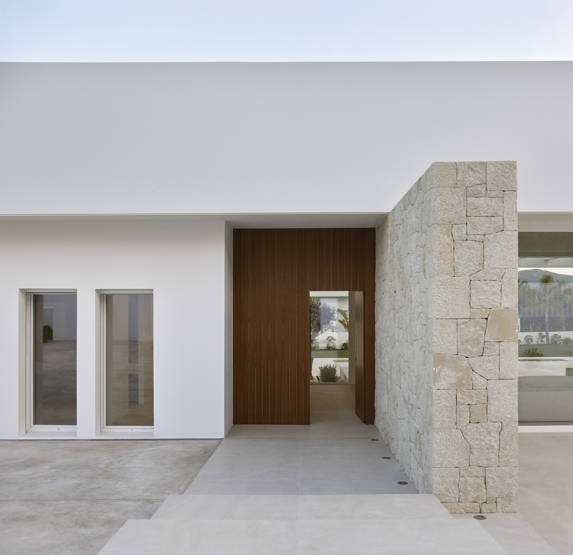 Covered entry with timber door and white stucco wall flanked by a limestone masonry column