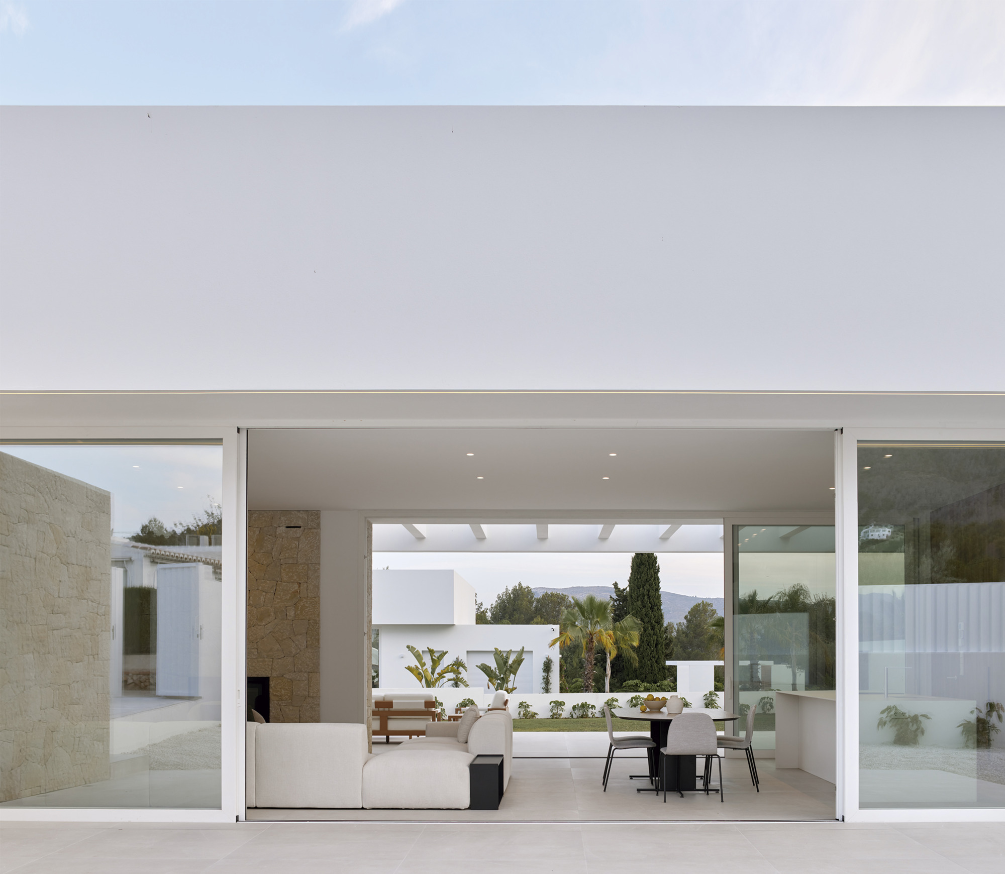 Open living pavilion with clerestory glazing framing courtyard plantings and cypress trees
