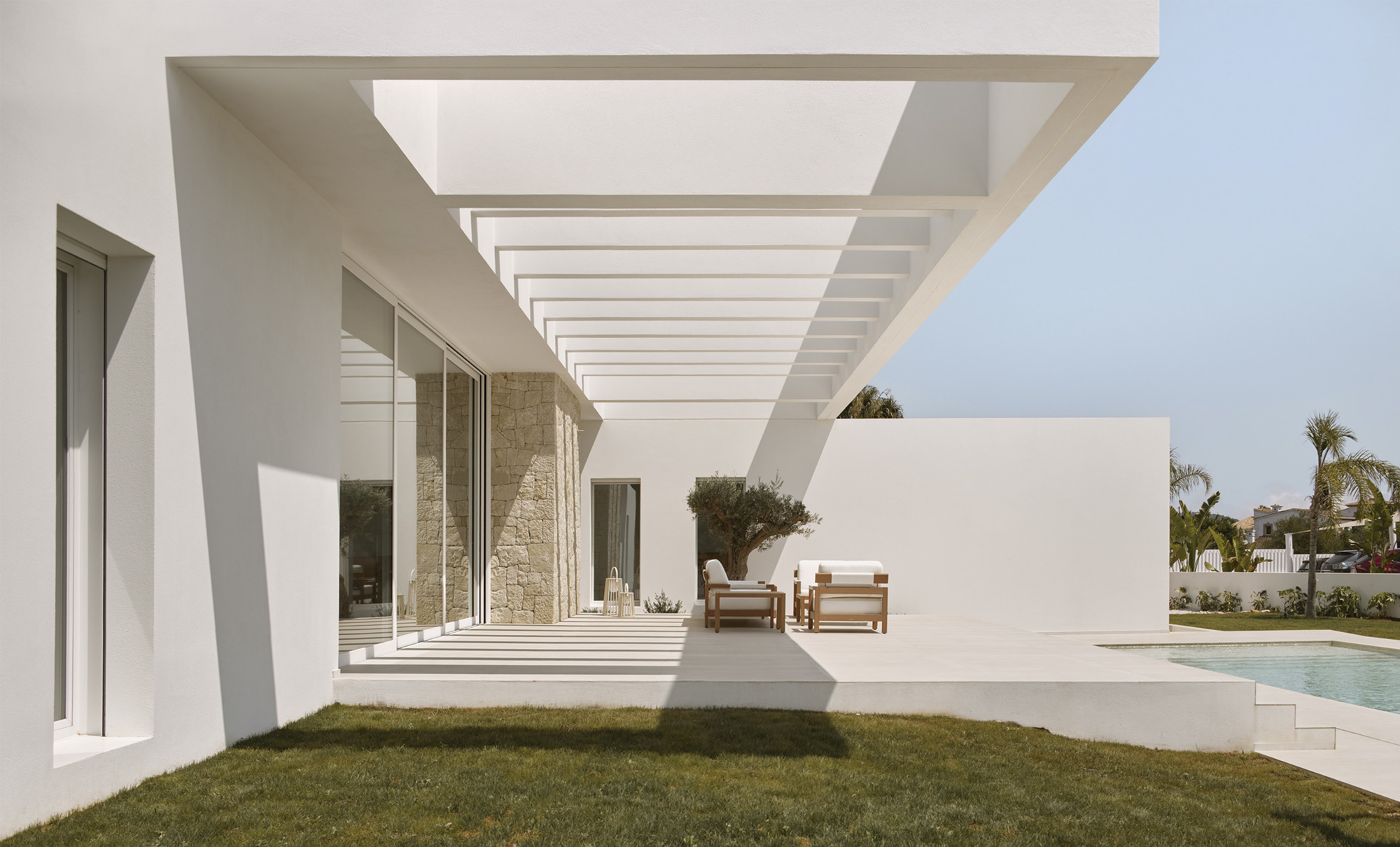 Slatted pergola casting shadow stripes across the terrace with lawn in the foreground