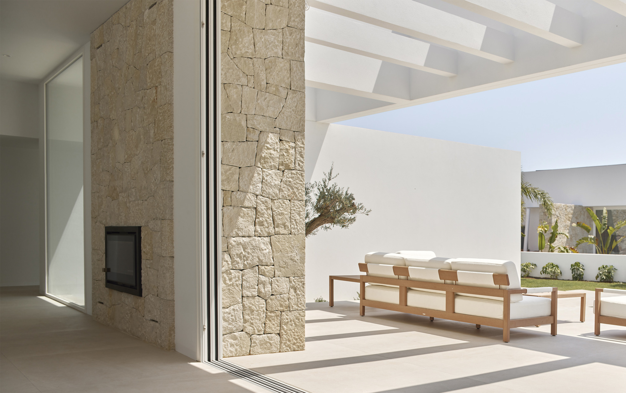 Interior threshold to poolside terrace with limestone fireplace wall and timber lounge chairs