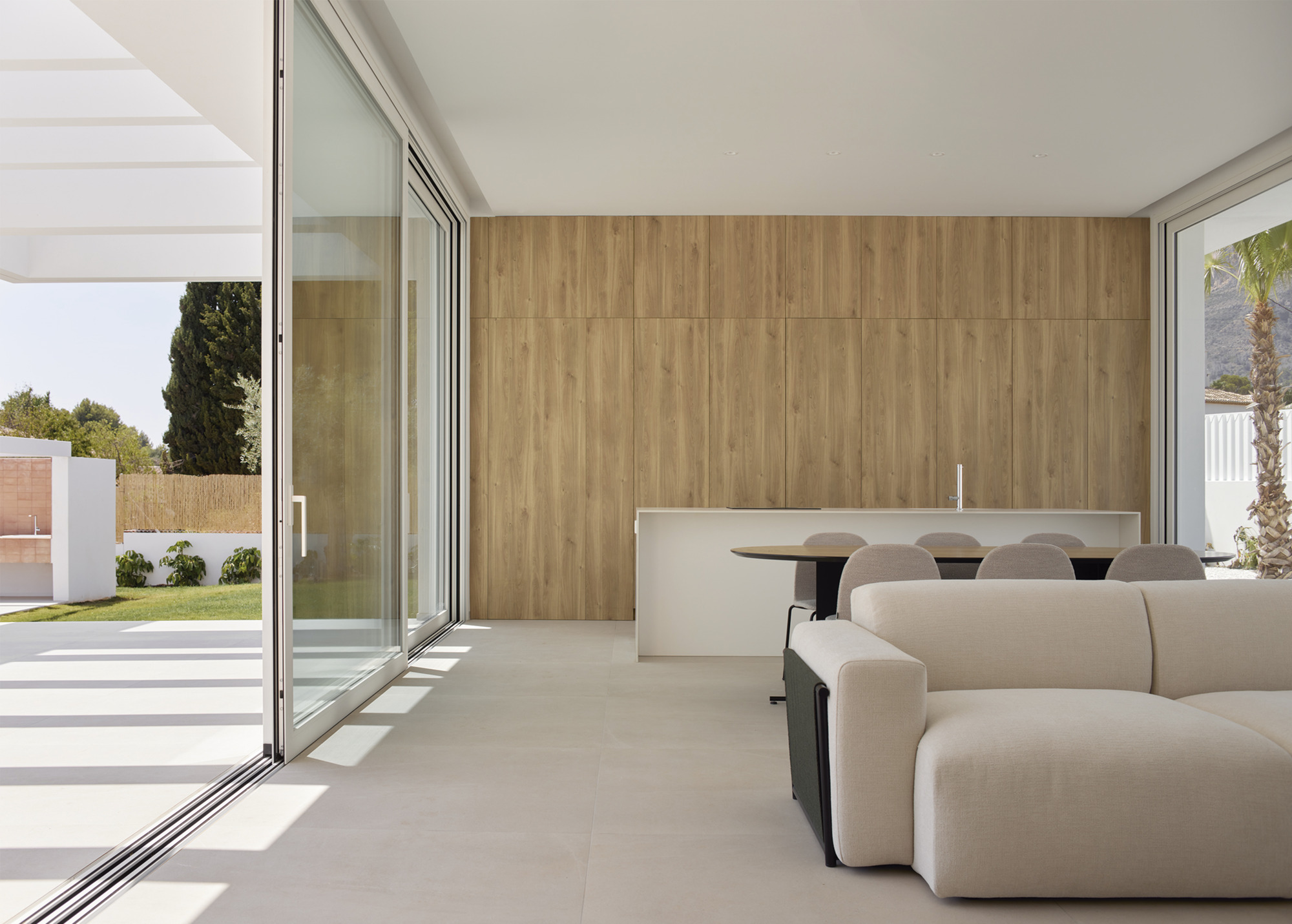 Open plan living space with floor-to-ceiling glass doors opening onto a garden with palm trees