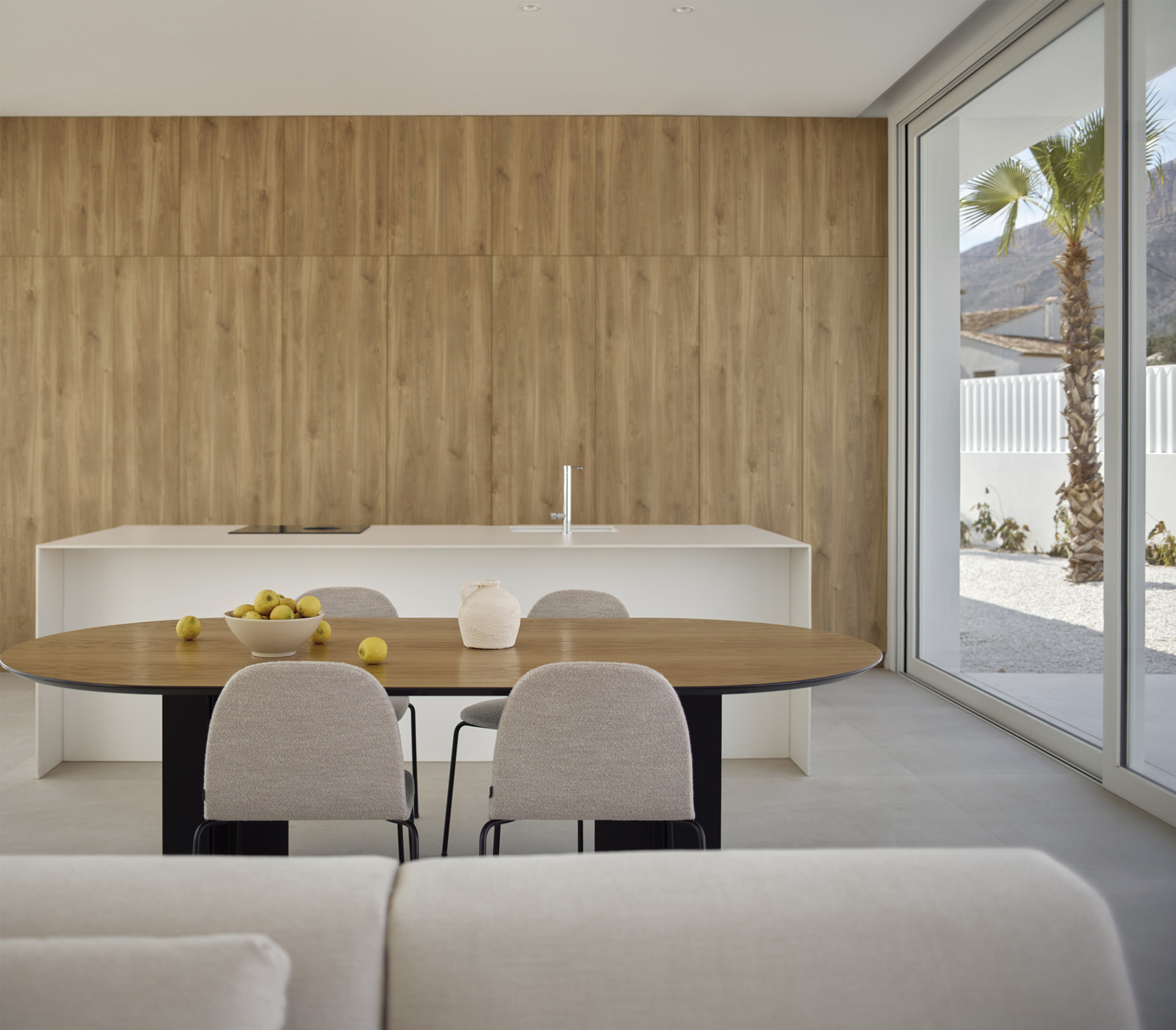 Dining area with round timber table and white island counter against a vertical wood-paneled wall