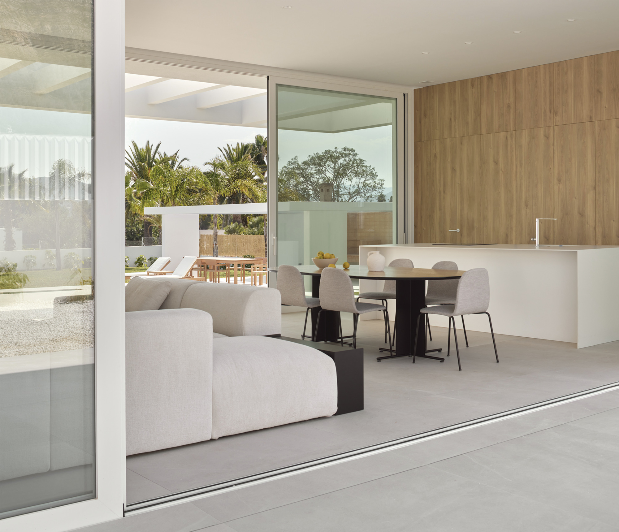 Living and dining space viewed through sliding glass doors with poolside terrace visible beyond