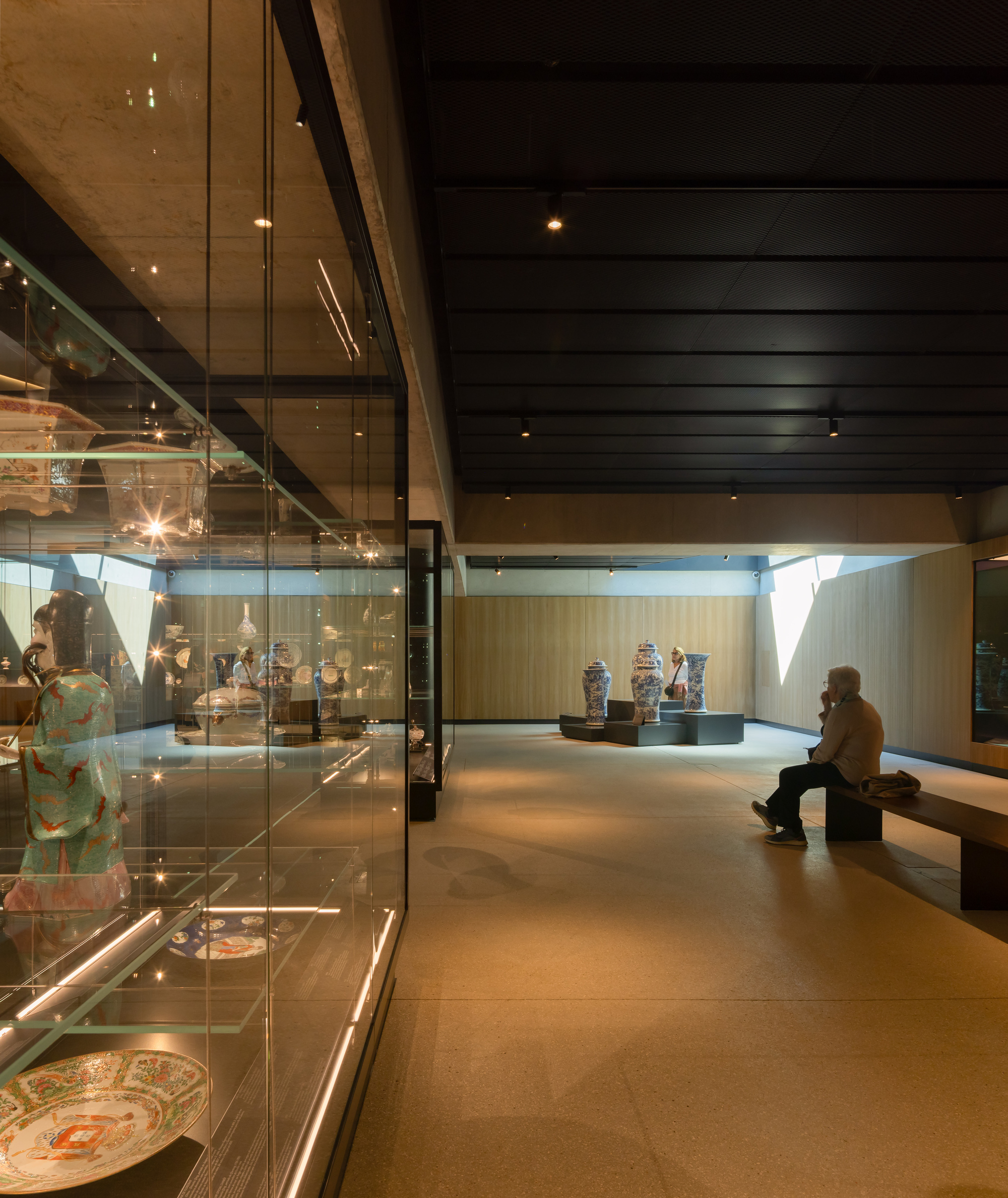 Gallery interior with glass display cases and seated visitor beneath black ceiling and timber wall