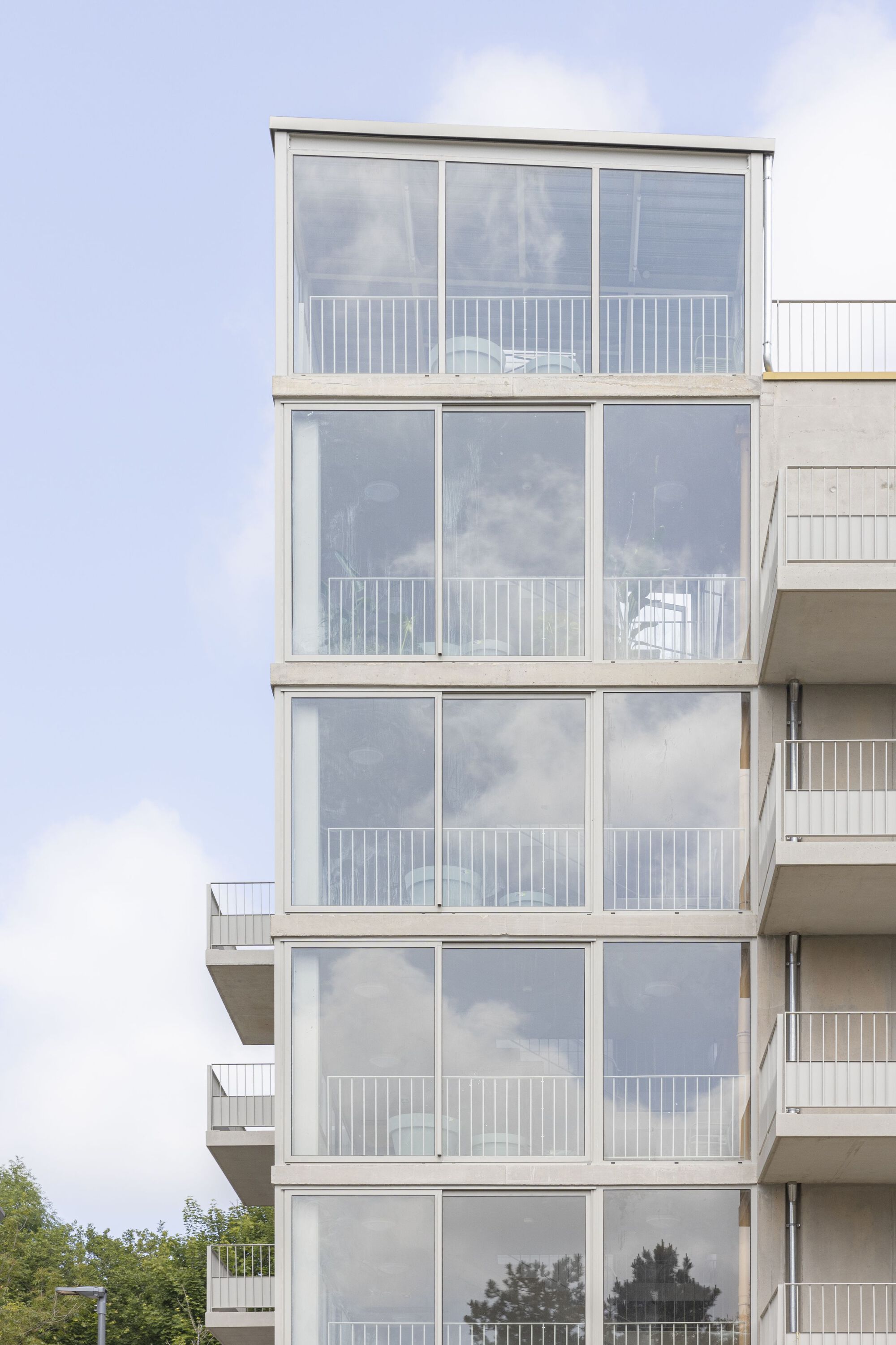 Stacked glazed balconies with white metal railings rising against a cloudy sky