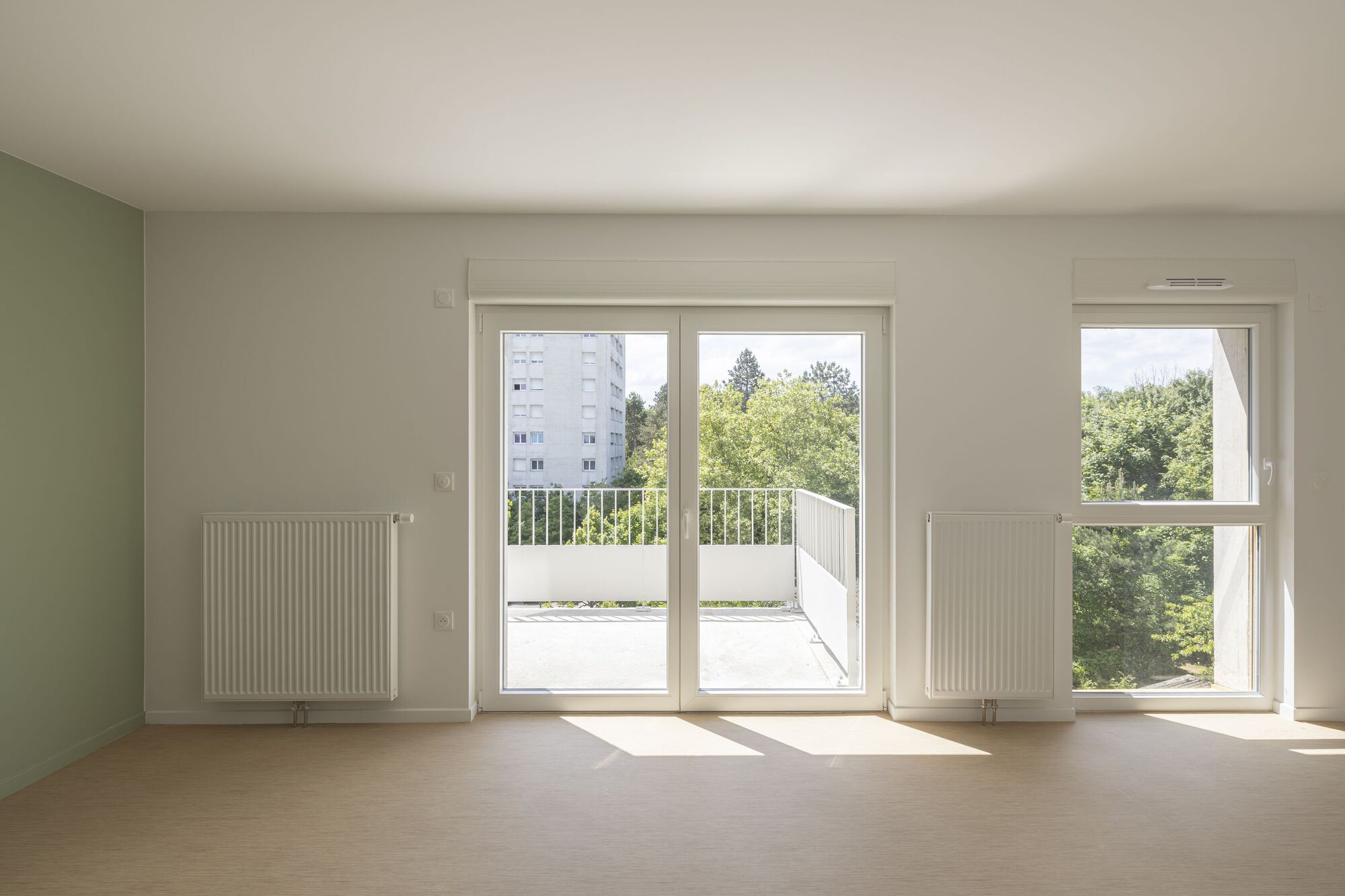 Bare interior room with pale wood flooring, wall-mounted radiators and sliding door to exterior balcony