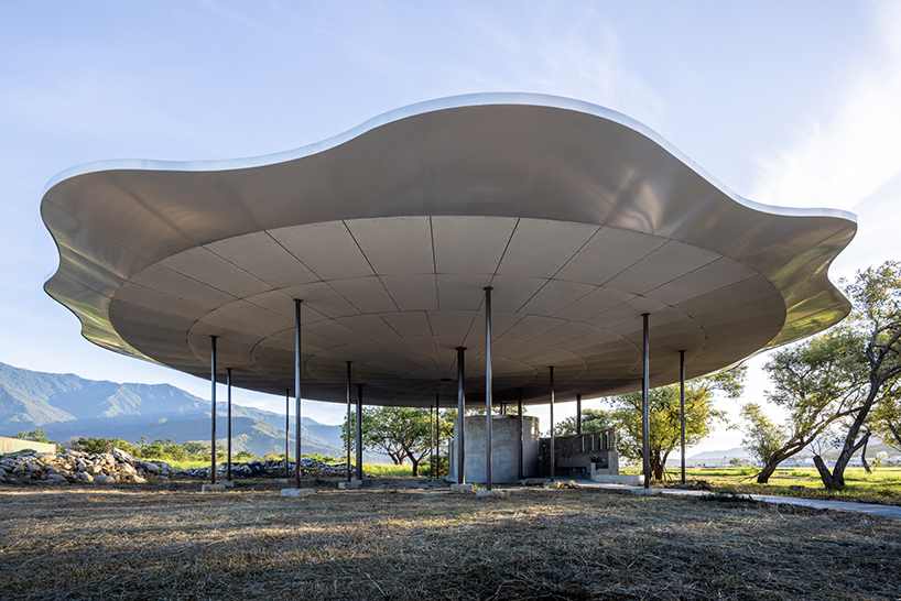 Undulating canopy roof supported by slender black columns with mountains and trees in the background