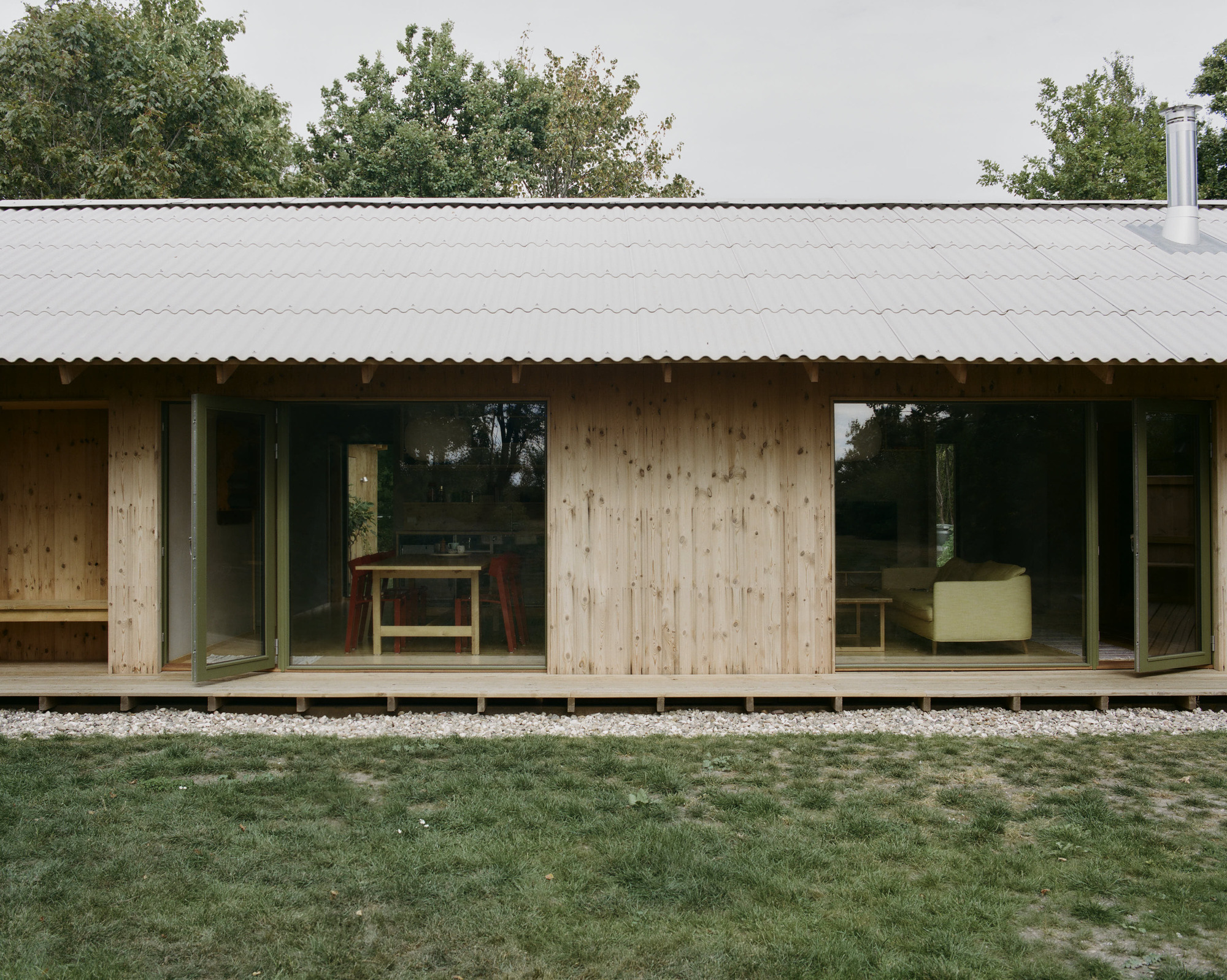 Light timber facade with sliding glass doors and corrugated metal roof above a gravel bed
