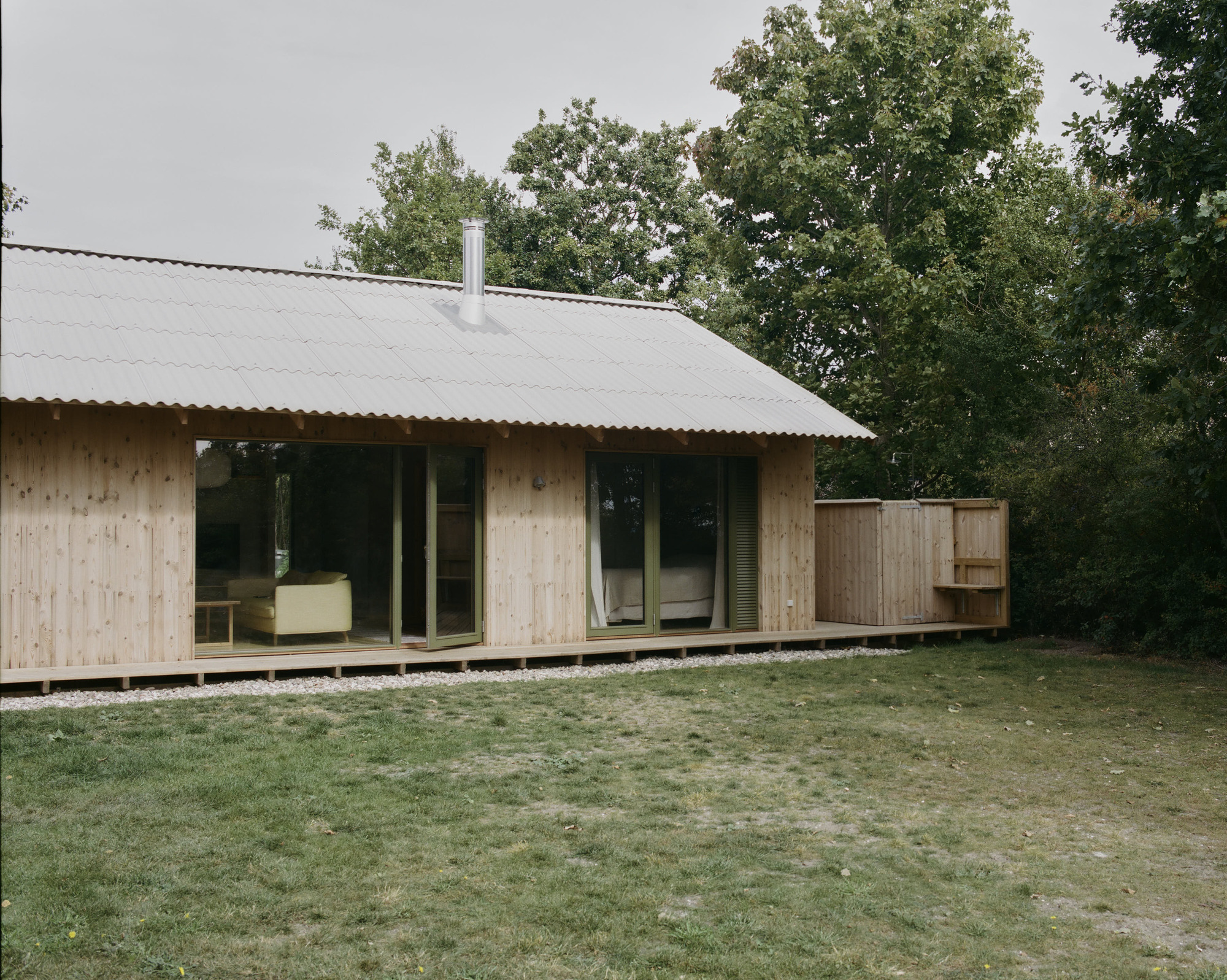 Corner view of timber pavilion with corrugated roof overhang and timber deck on gravel