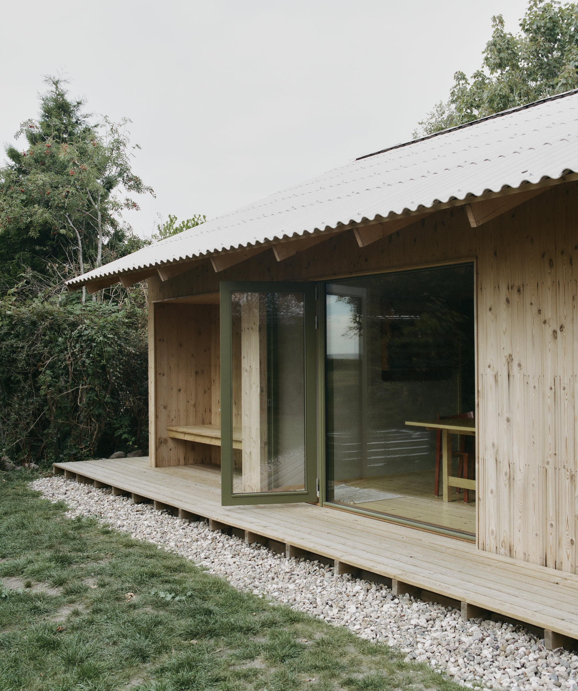 Covered timber deck with built-in bench and sliding doors under corrugated metal eave