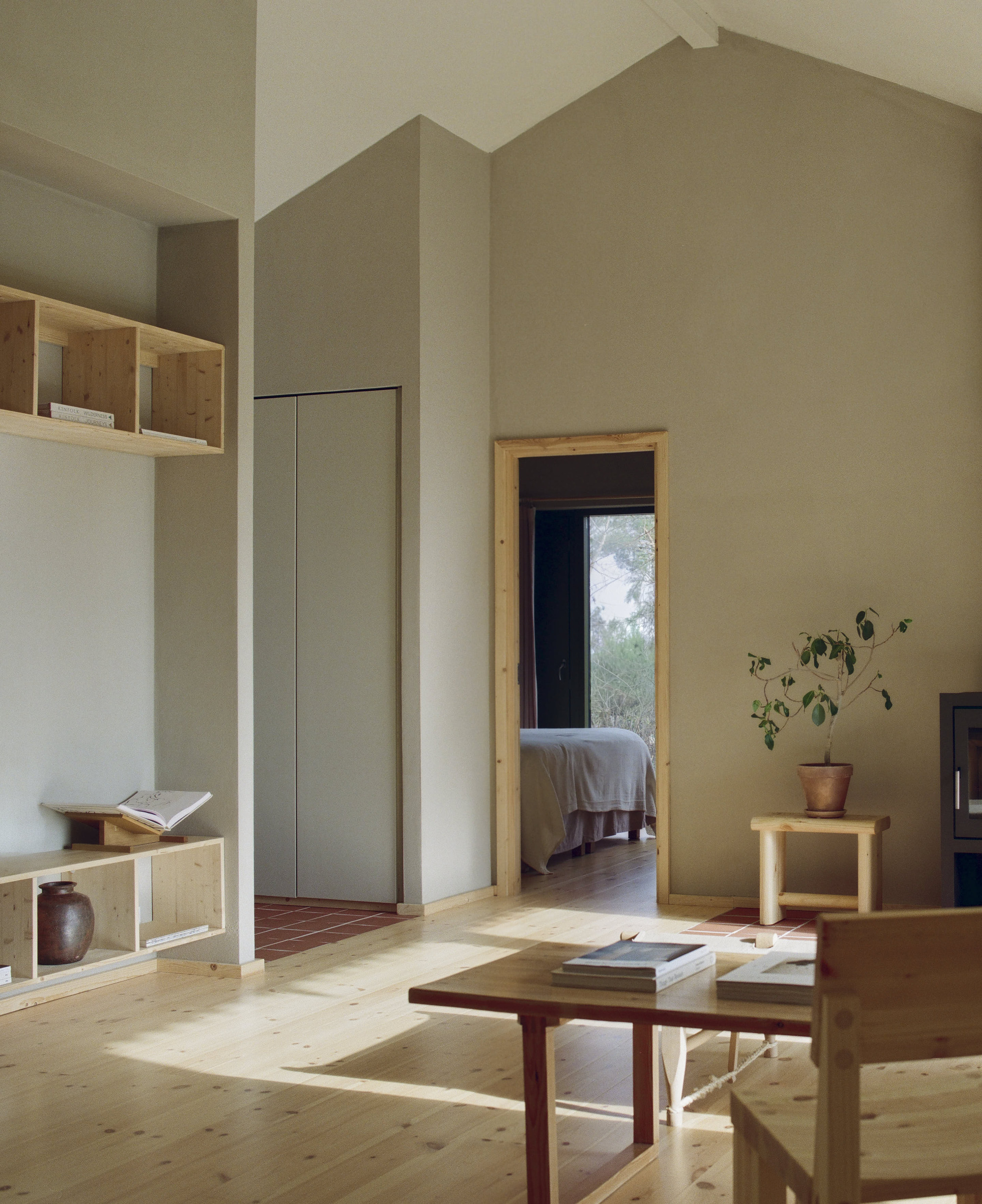 Living room with pale plaster walls and timber joinery looking through a doorway to a bedroom
