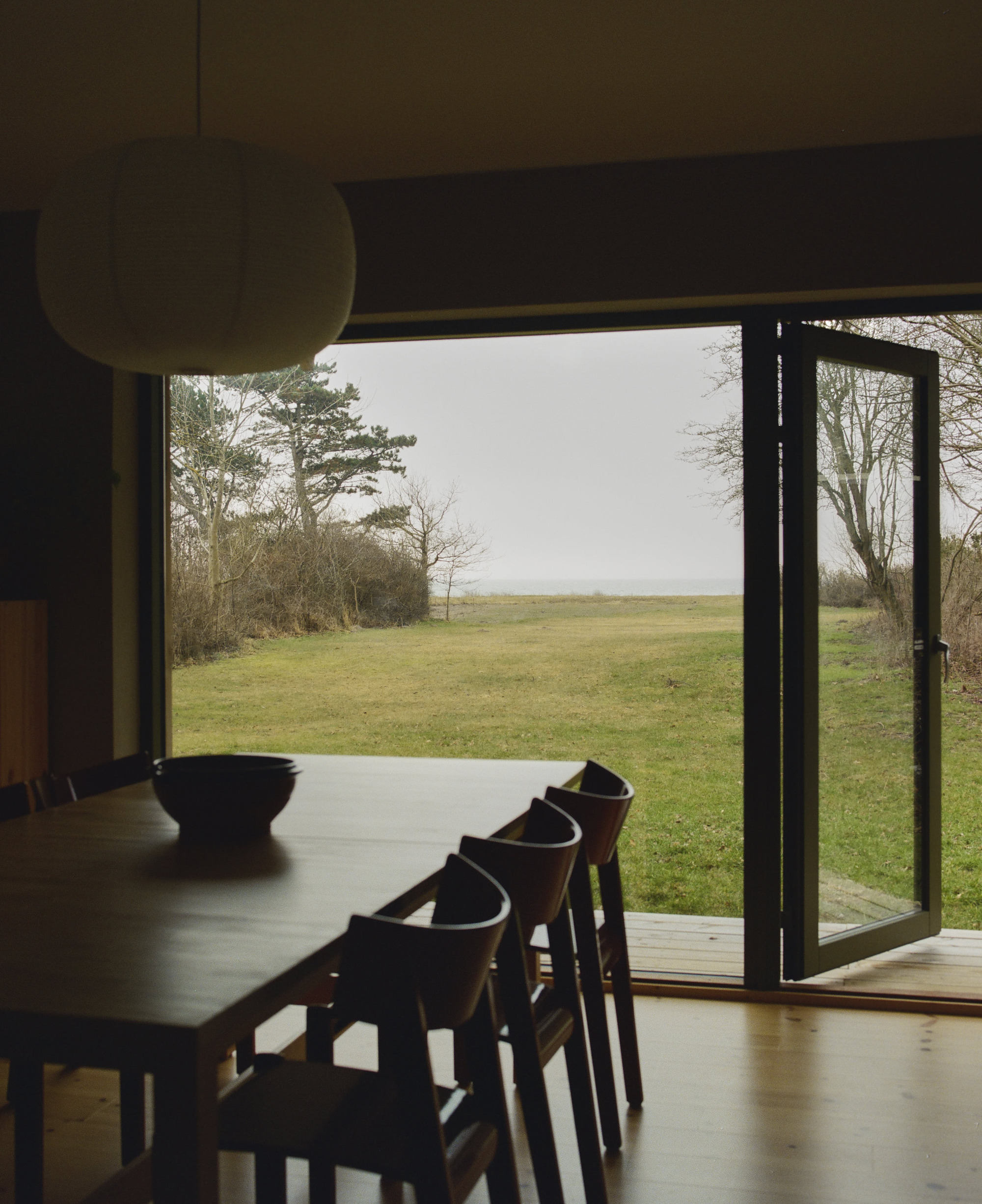 Dining table and chairs framing an open glazed door to the grassy field beyond