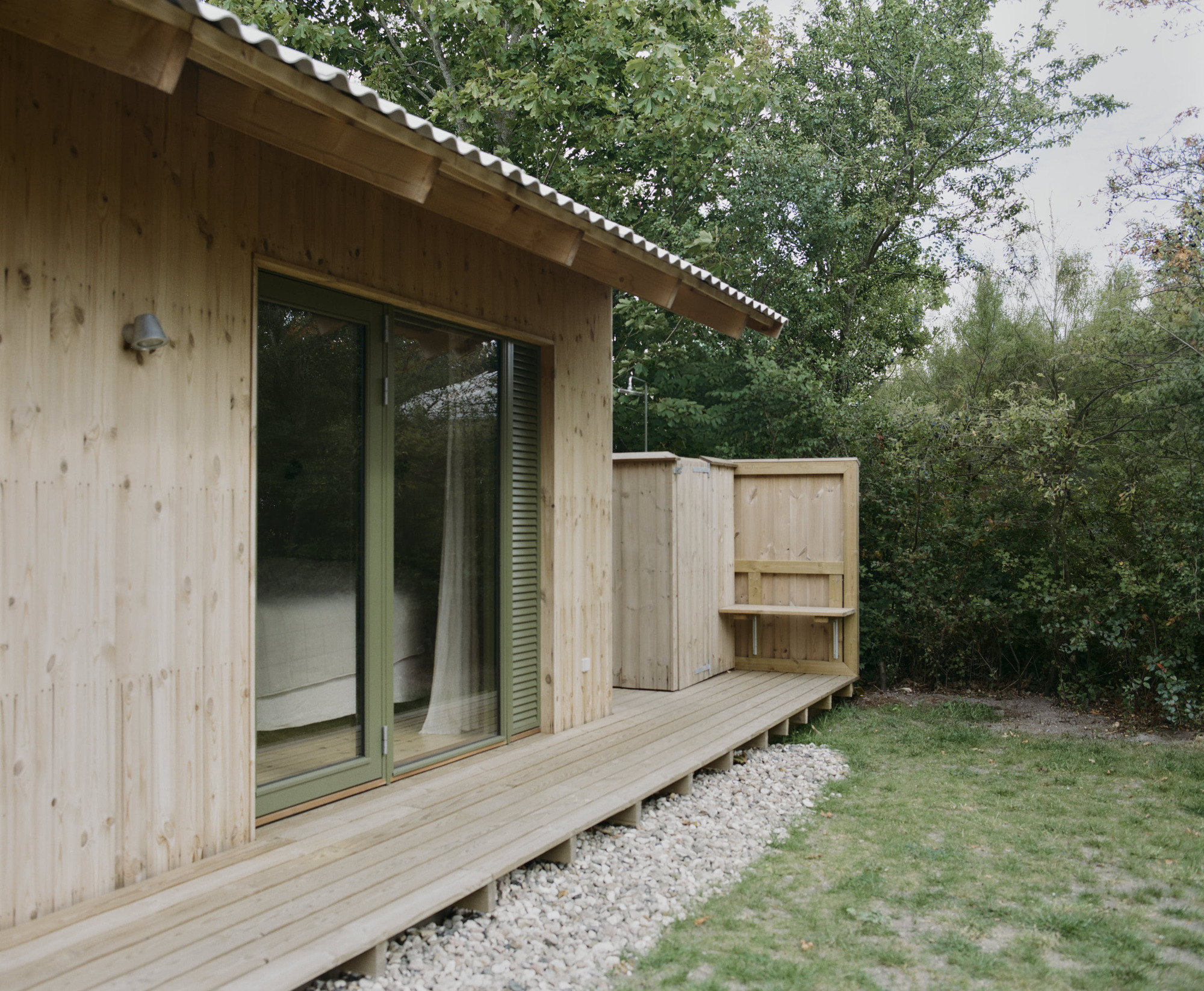 Exterior view of timber-clad volume with corrugated metal roof and sliding glass doors to deck
