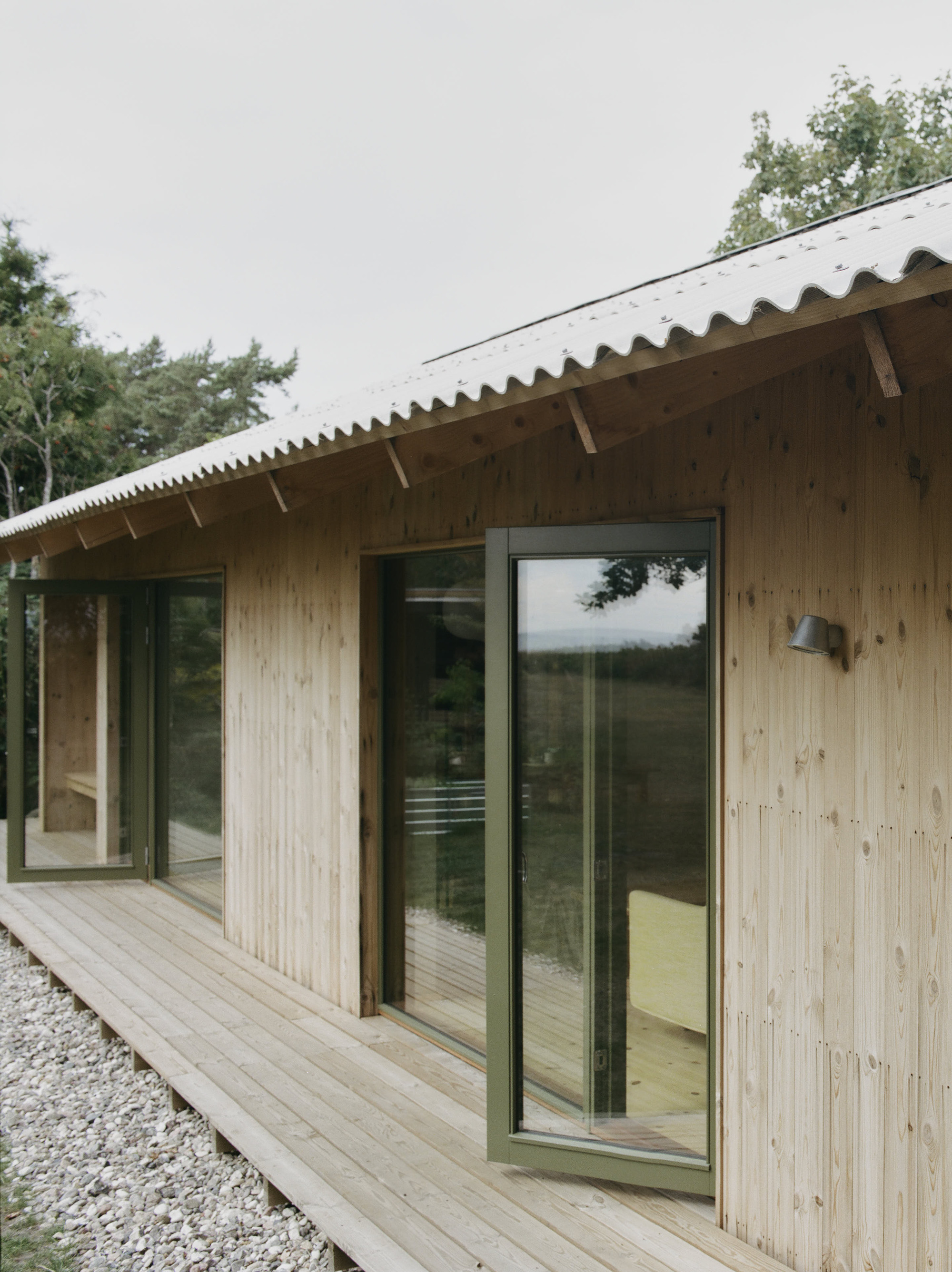 Facade showing vertical timber cladding with dark-framed glazing beneath a scalloped metal roof
