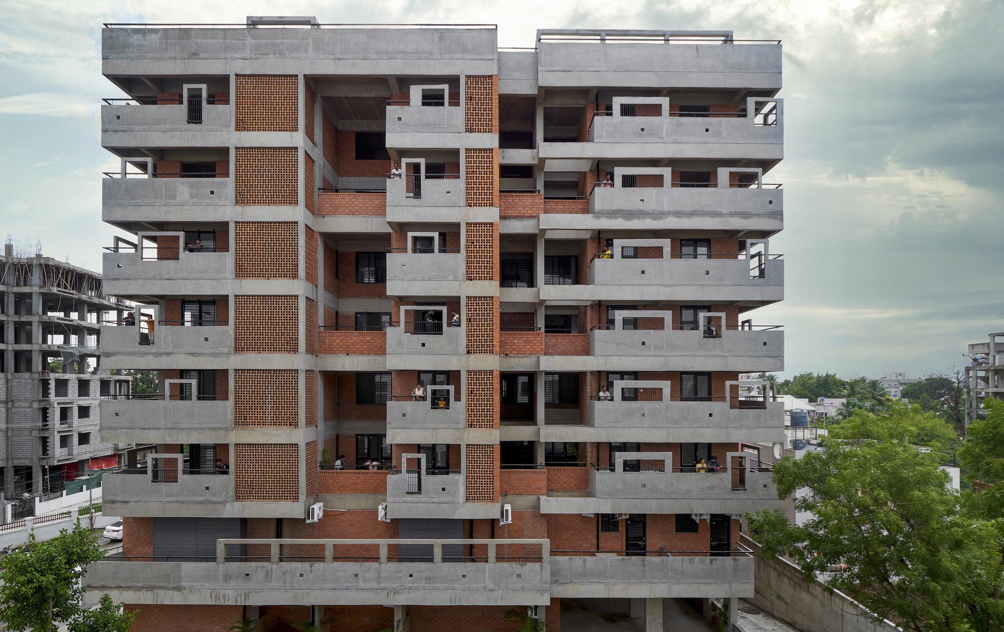 Multistory residential facade with concrete balconies and terracotta brick screens under a cloudy sky