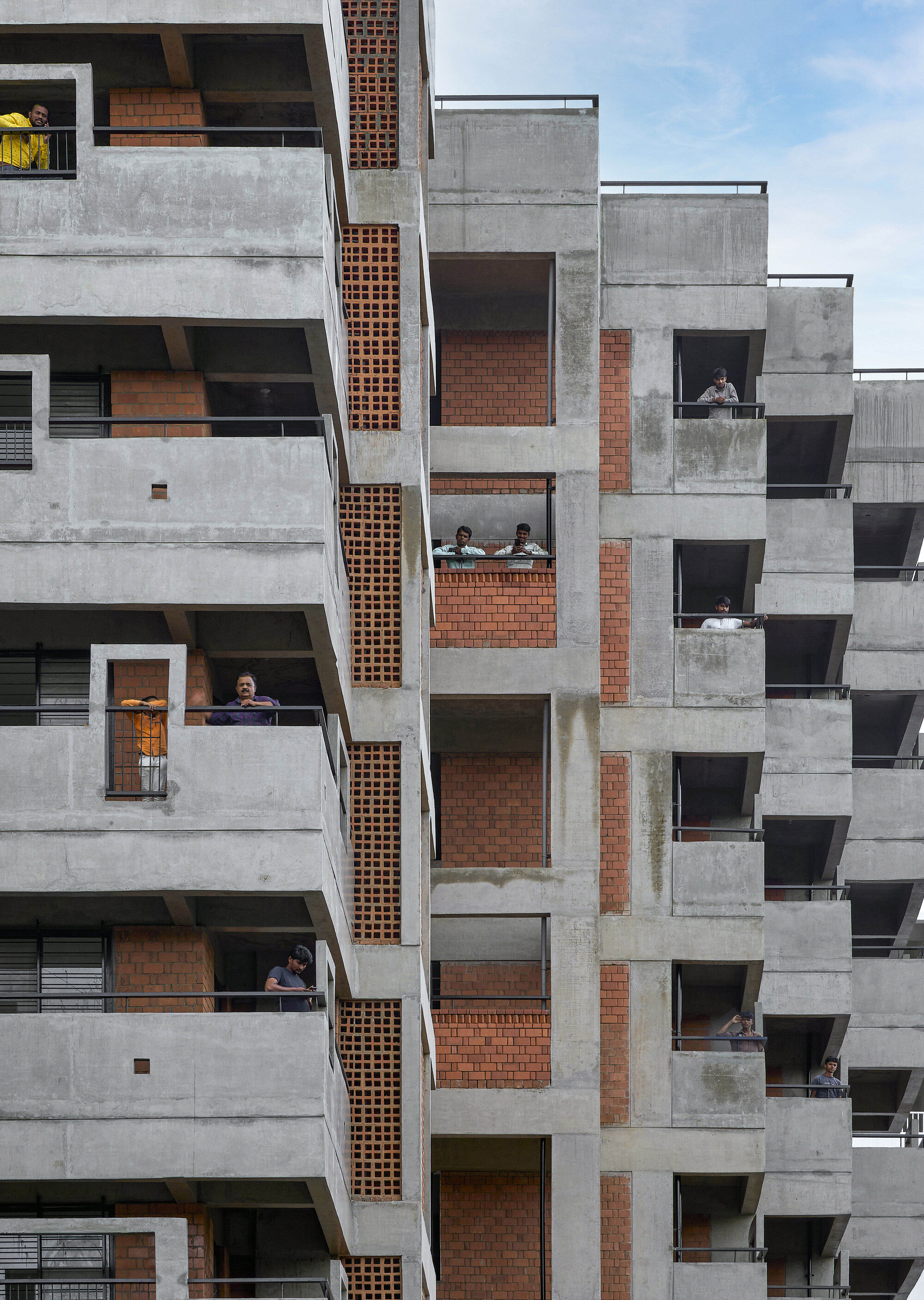 Staggered concrete balconies with exposed brick infill and residents visible in the window openings