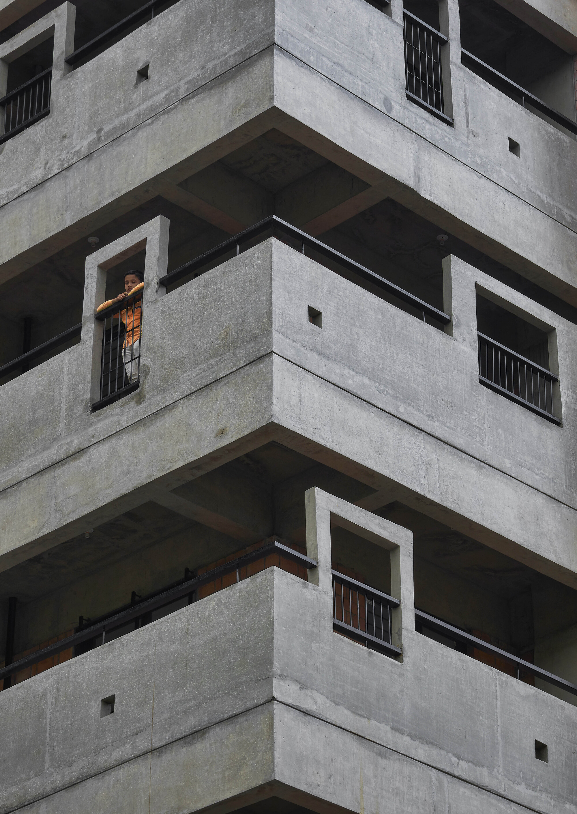 Corner detail of stacked concrete balconies with deep recesses and a resident in the window