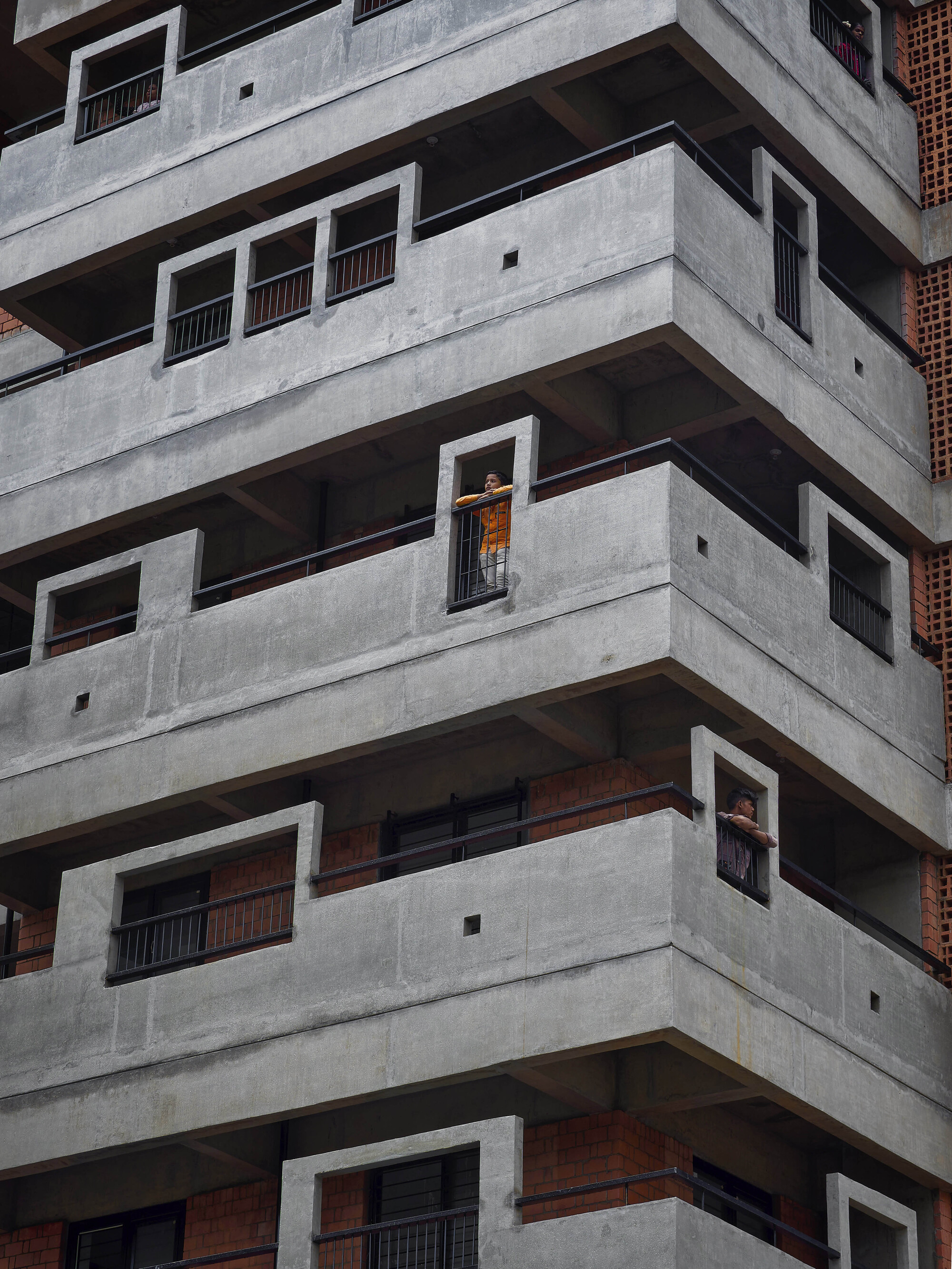Stacked concrete balconies with deep recesses and a resident visible in one window opening