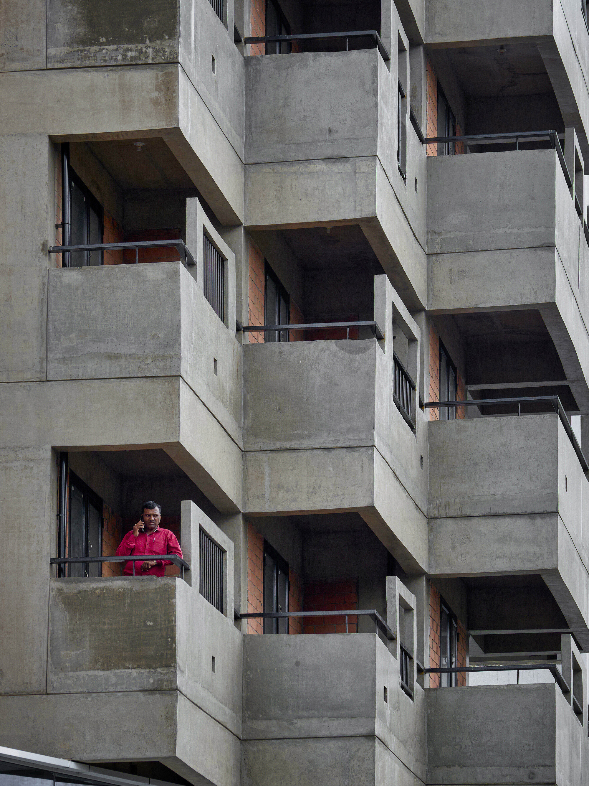 Concrete balconies with metal railings and exposed brick walls where a resident in red stands looking out