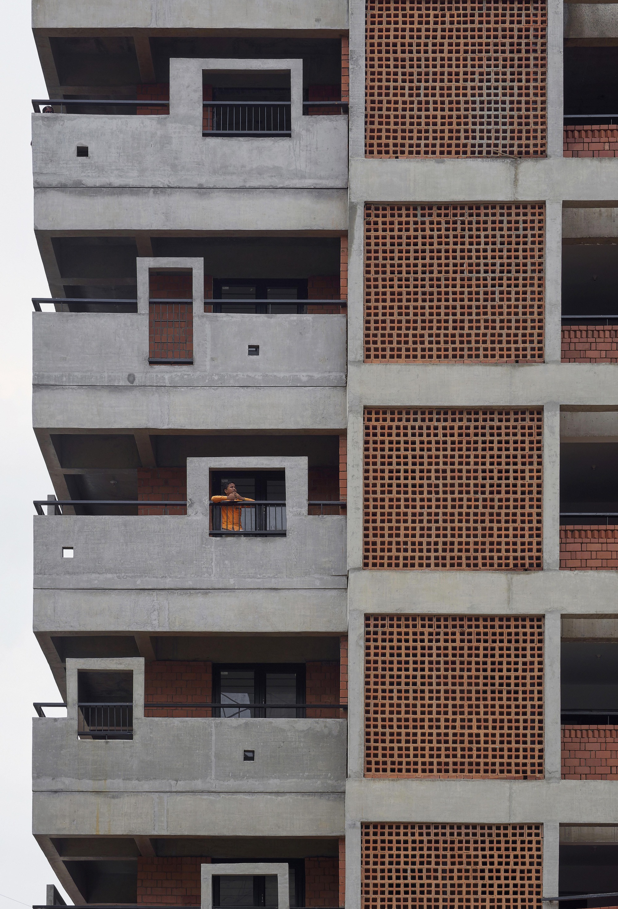Stacked concrete balconies with terracotta brick panels where one resident leans on a railing