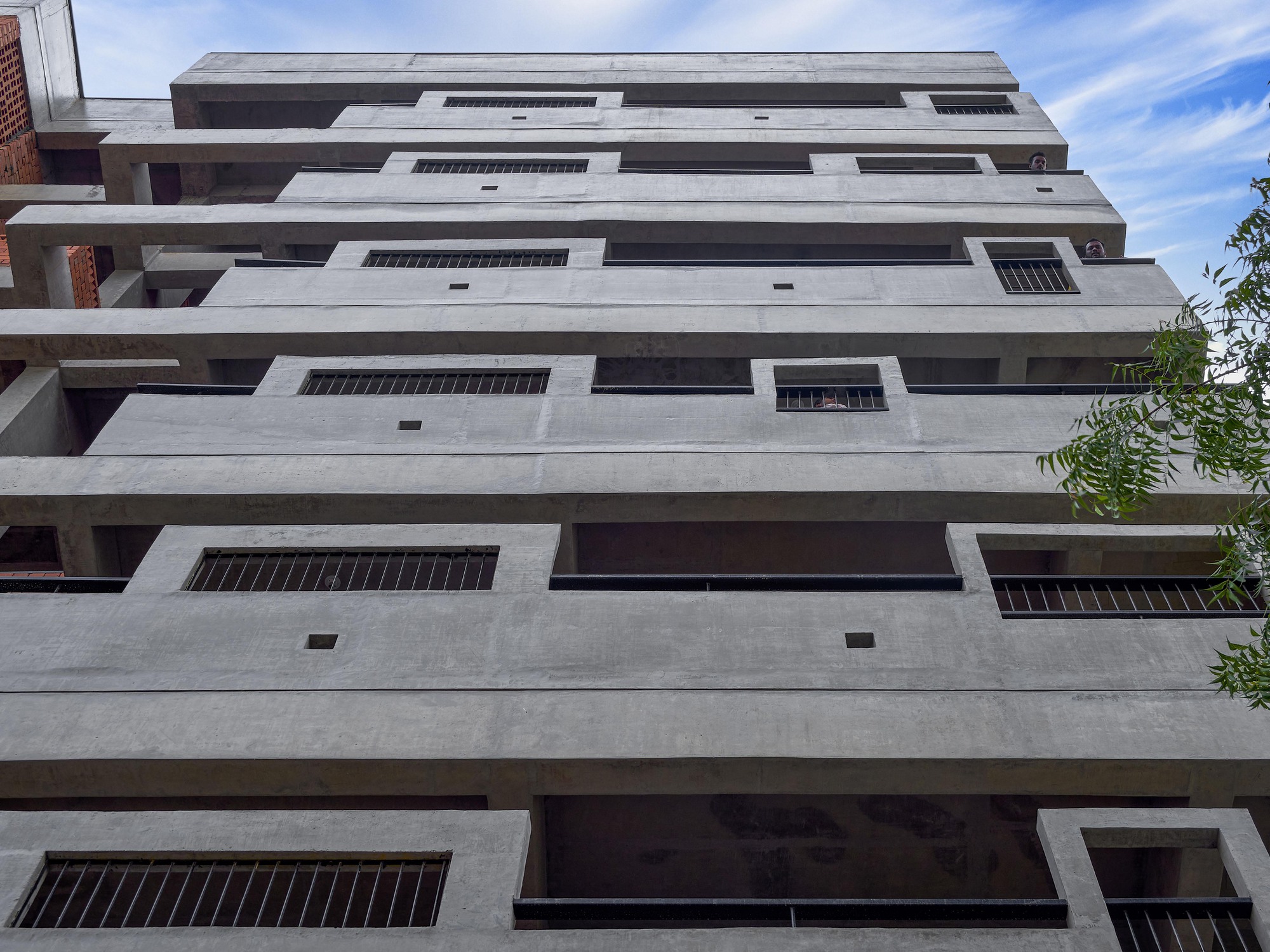 Ground-up view of the stepped concrete facade with deep balconies under a bright blue sky