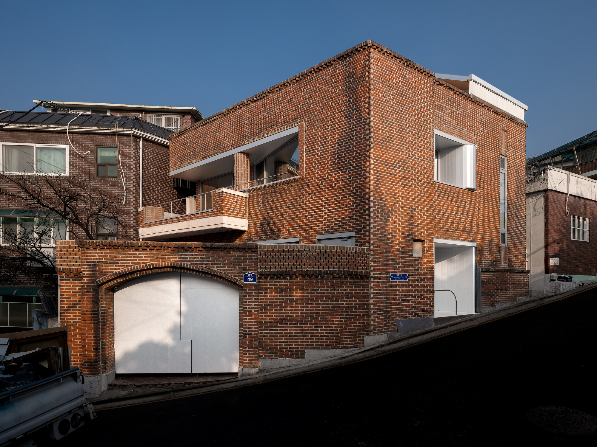 Corner view of the red brick building with recessed balcony and arched ground-level garage doors in late afternoon