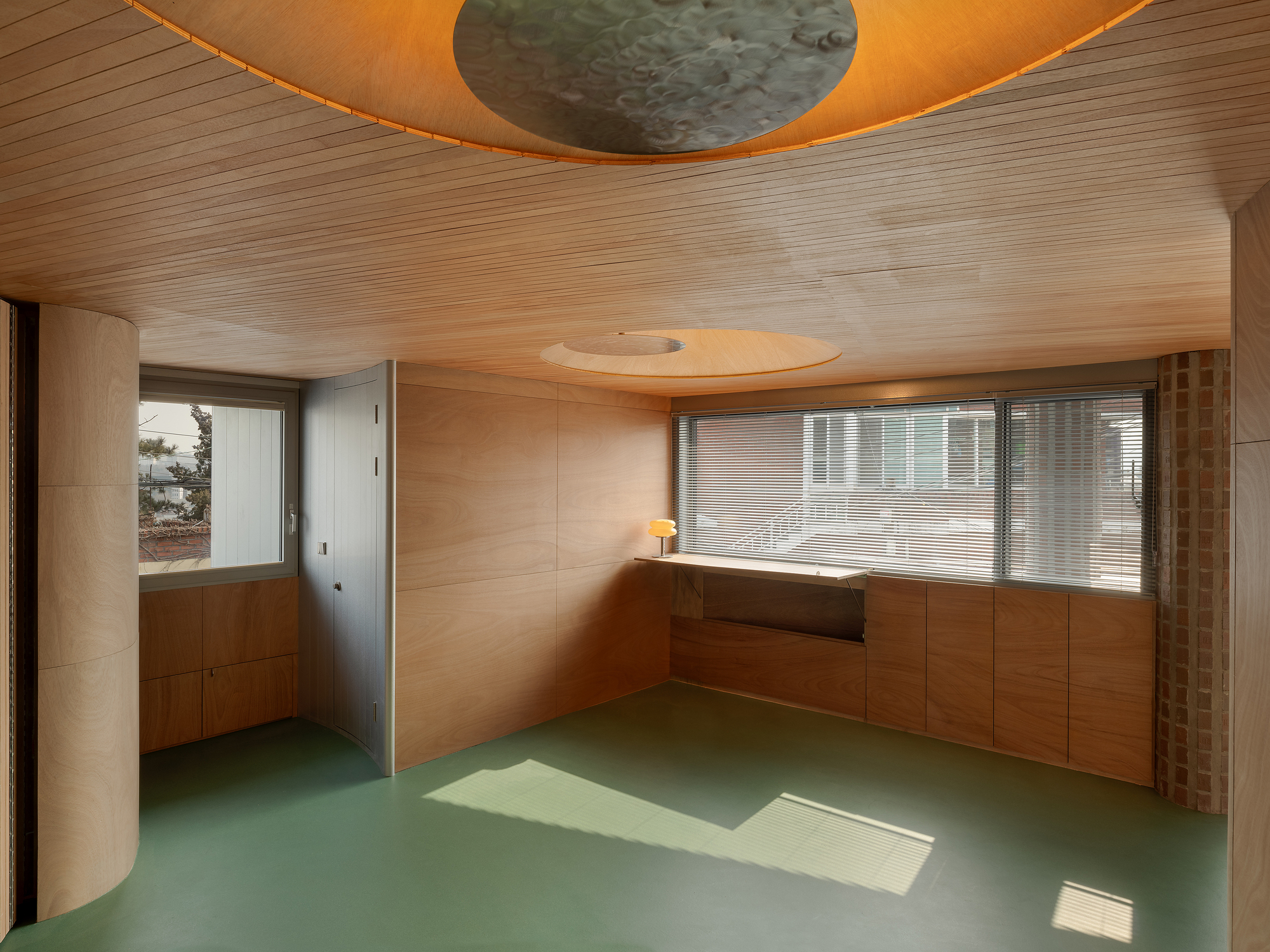 Interior room with timber-lined ceiling, green rubber floor and circular skylight above window seat