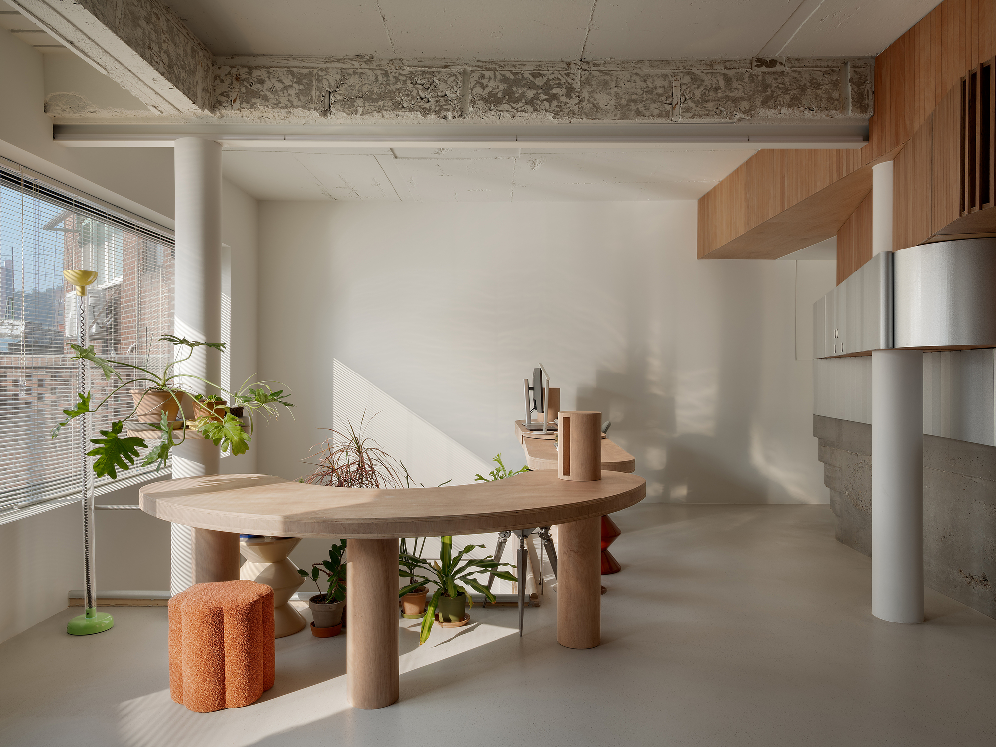 Workspace with sculptural timber table and potted plants in afternoon sunlight beneath exposed concrete beam