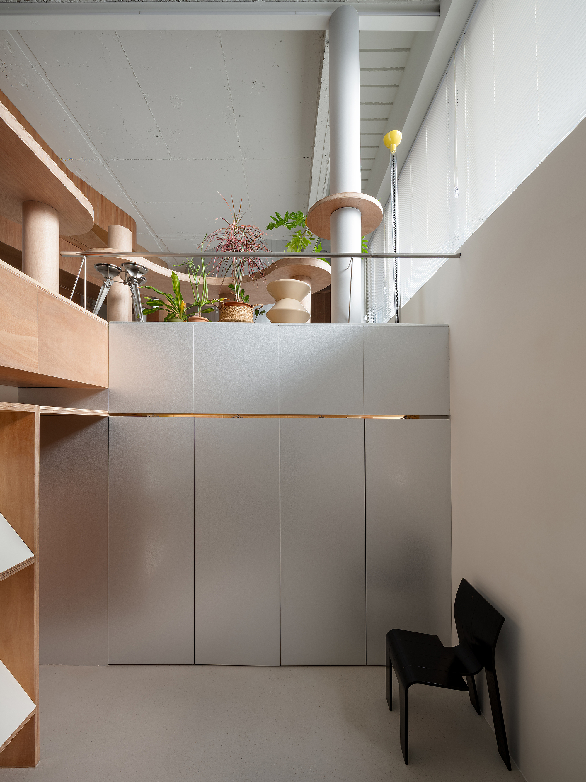 Double-height space with mezzanine storage displaying potted plants above grey paneled cabinetry and a white column