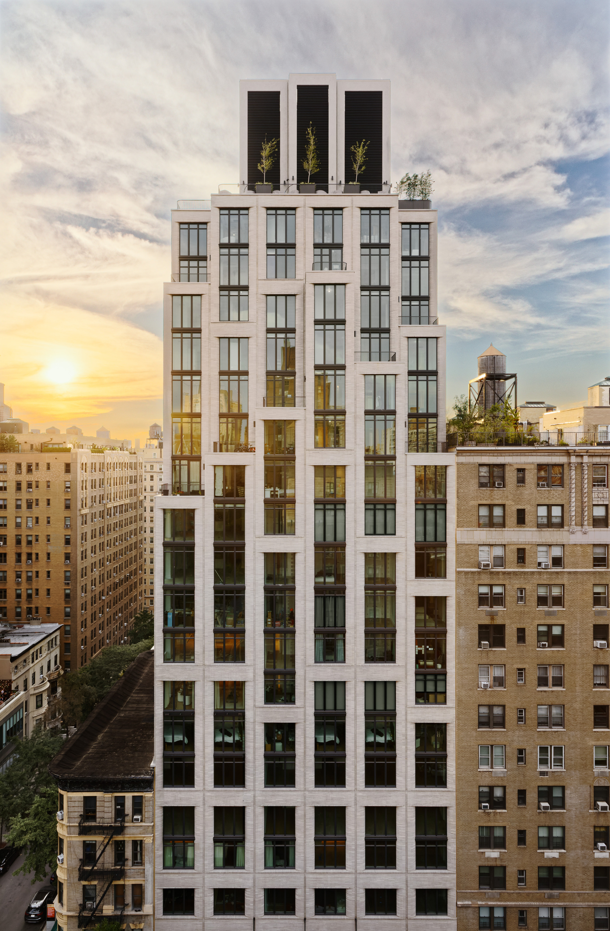 Full facade view showing the white frame grid with three dark rooftop volumes and planted terraces