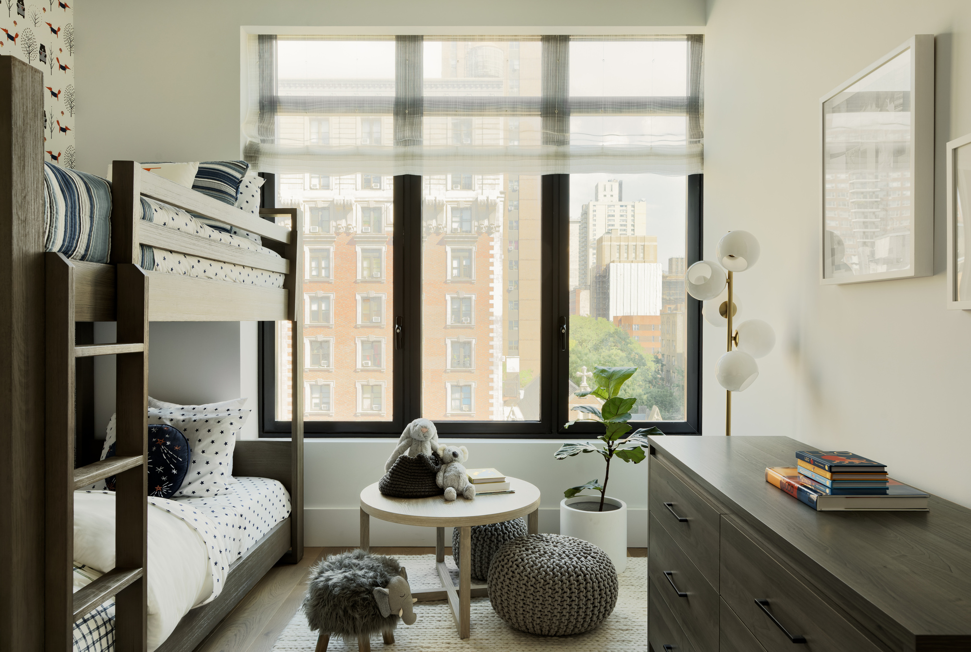 Bedroom with bunk bed and black-framed windows overlooking urban apartment buildings through sheer roller shades