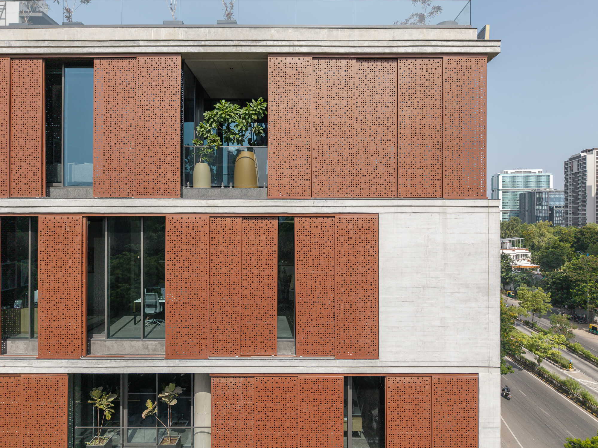 Perforated terracotta panel facade with sliding screens framing balconies and glazed openings under clear blue sky