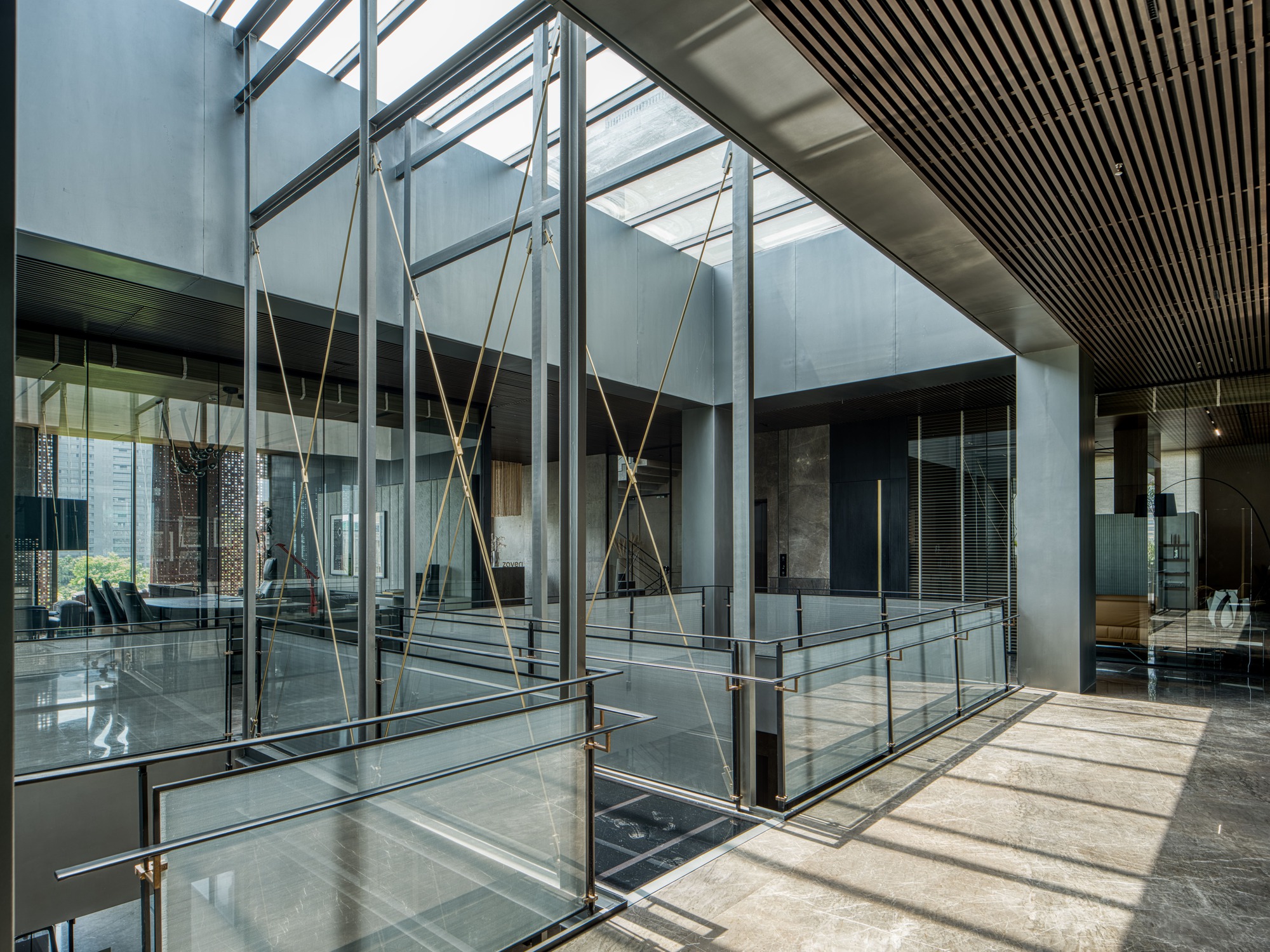 Glass-enclosed bridge with brass tension cables crossing an interior courtyard under a translucent skylight