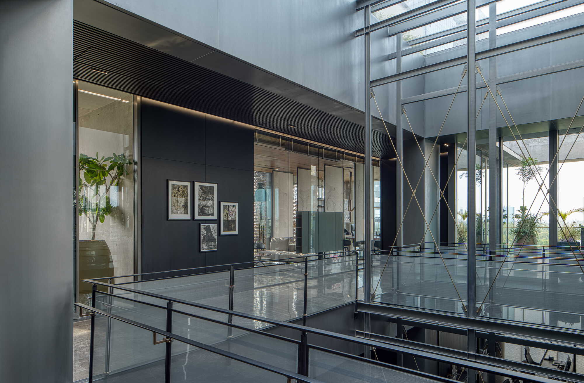 Interior walkway with glass railings and brass cable structure overlooking dark paneled walls and hanging plants