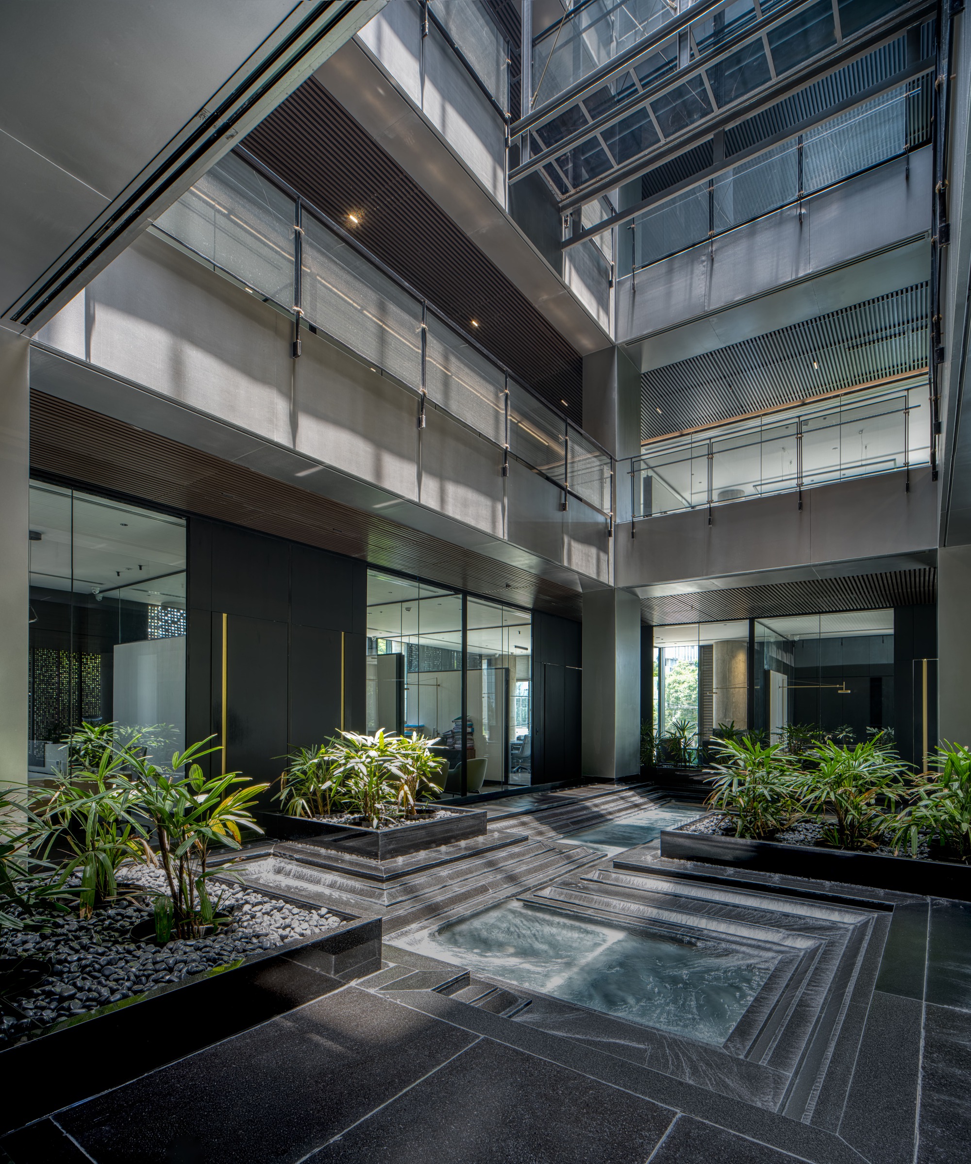 Interior courtyard with shallow reflecting pool surrounded by planted beds and glass-walled volumes above