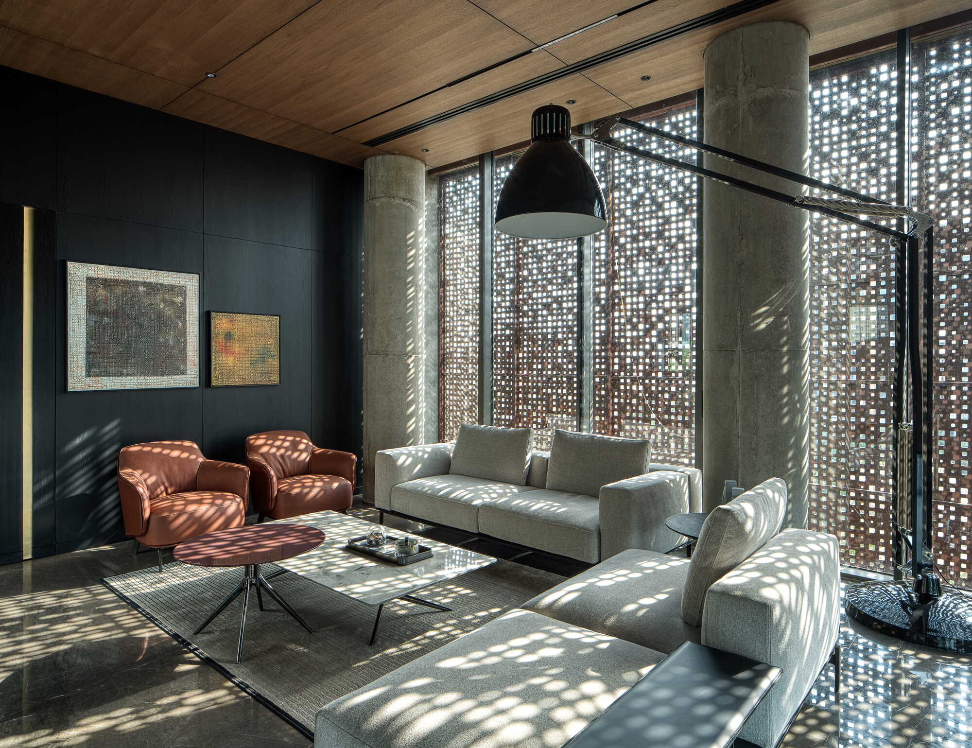 Double-height lounge with perforated metal facade, exposed concrete columns and dappled light patterns across timber ceiling
