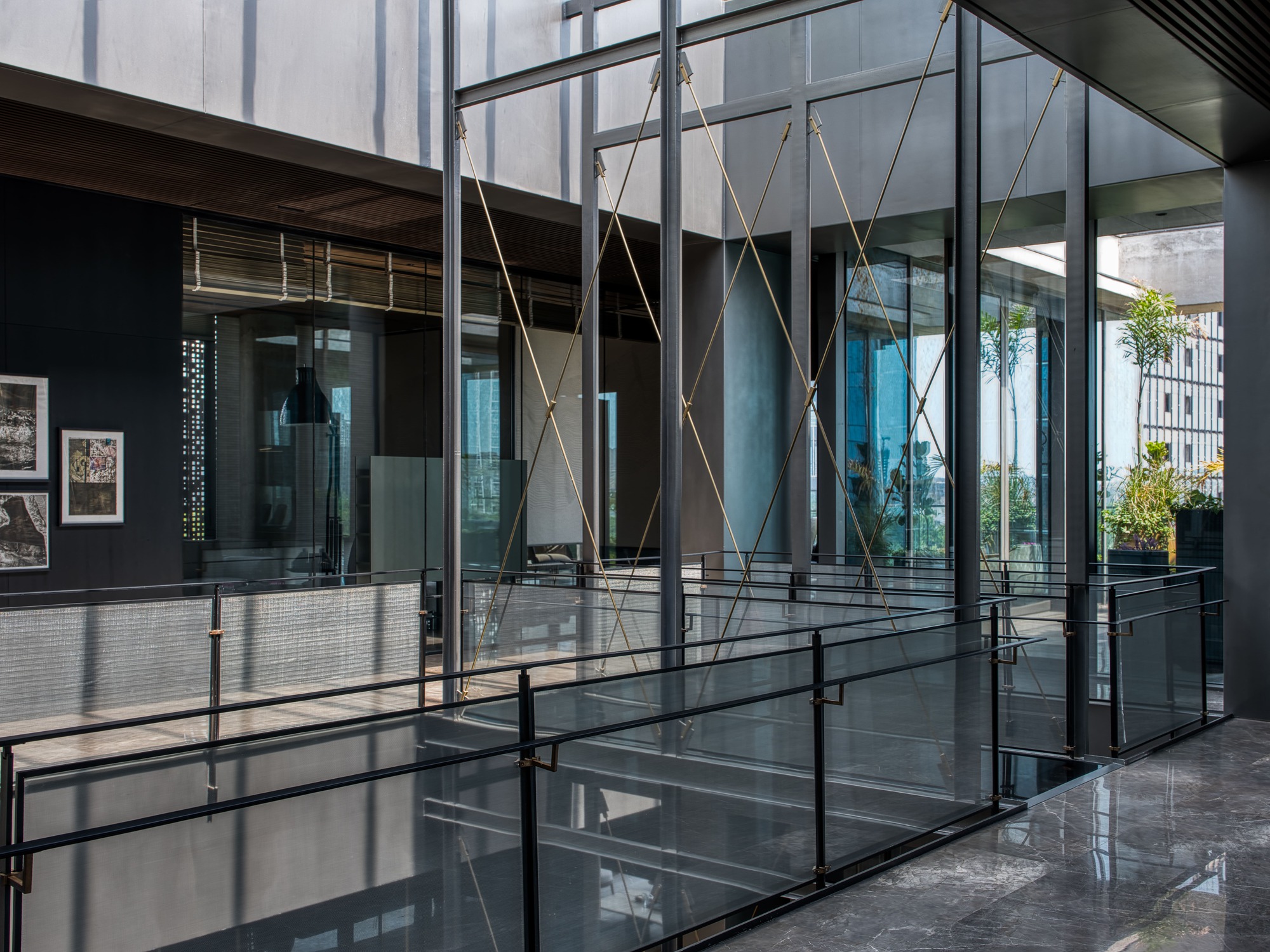 Glass-enclosed atrium with suspended rope bracing and steel walkways connecting interior volumes under overcast skies