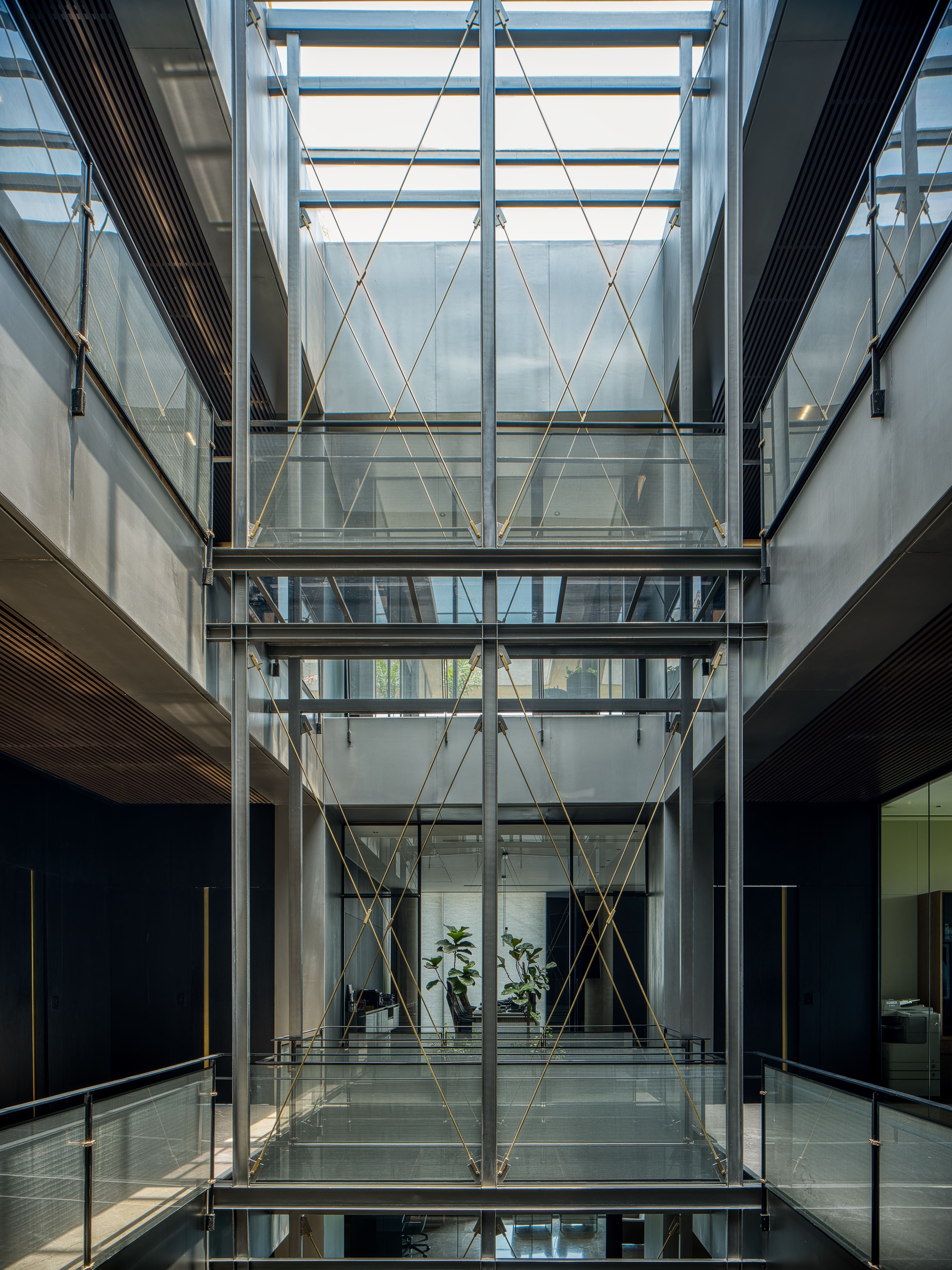 Central glazed void with diagonal rope tensioners spanning between steel-framed floors and planted terraces visible beyond