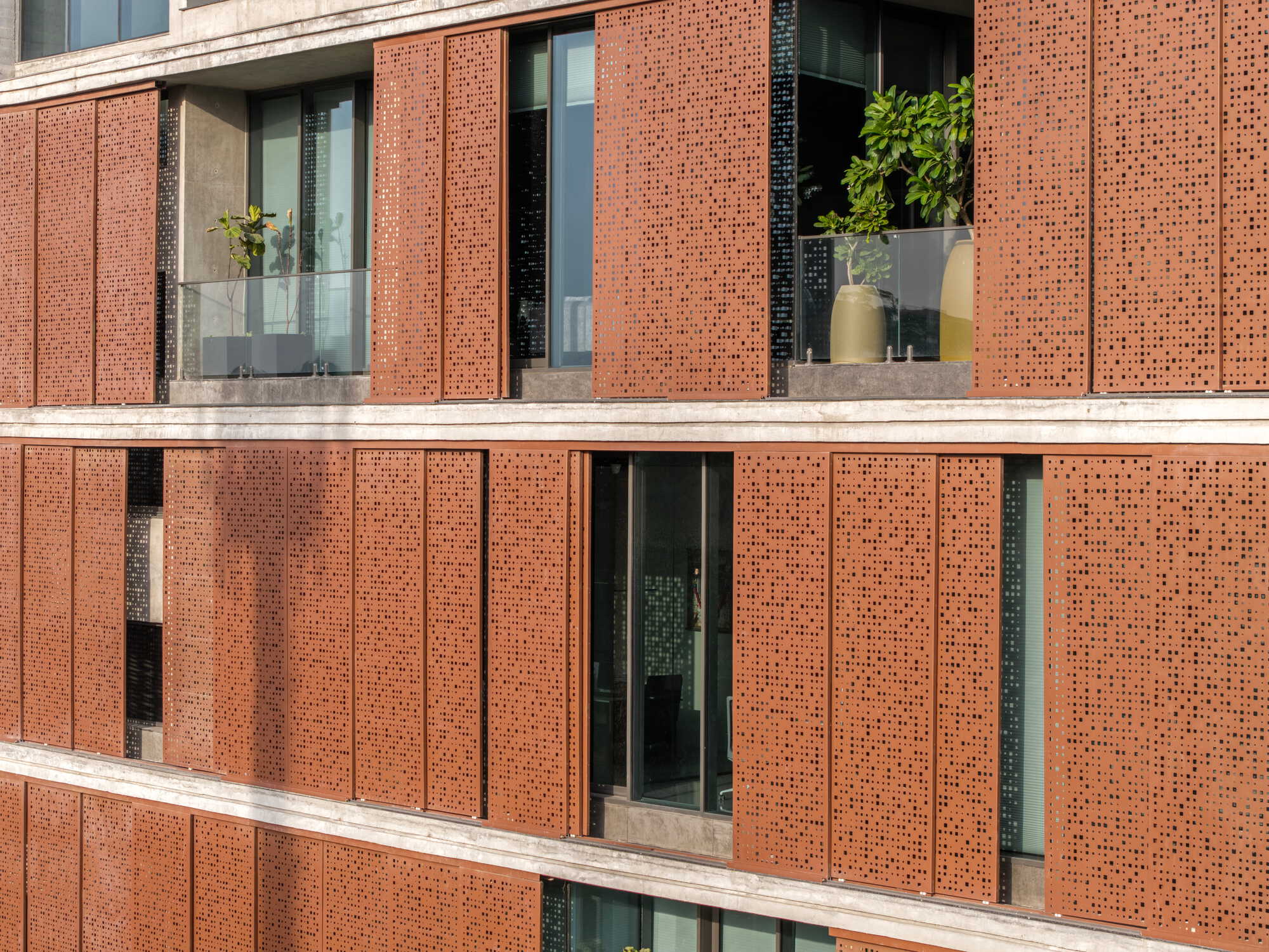 Facade detail showing perforated terracotta panels alternating with glass balconies and concrete floor slabs